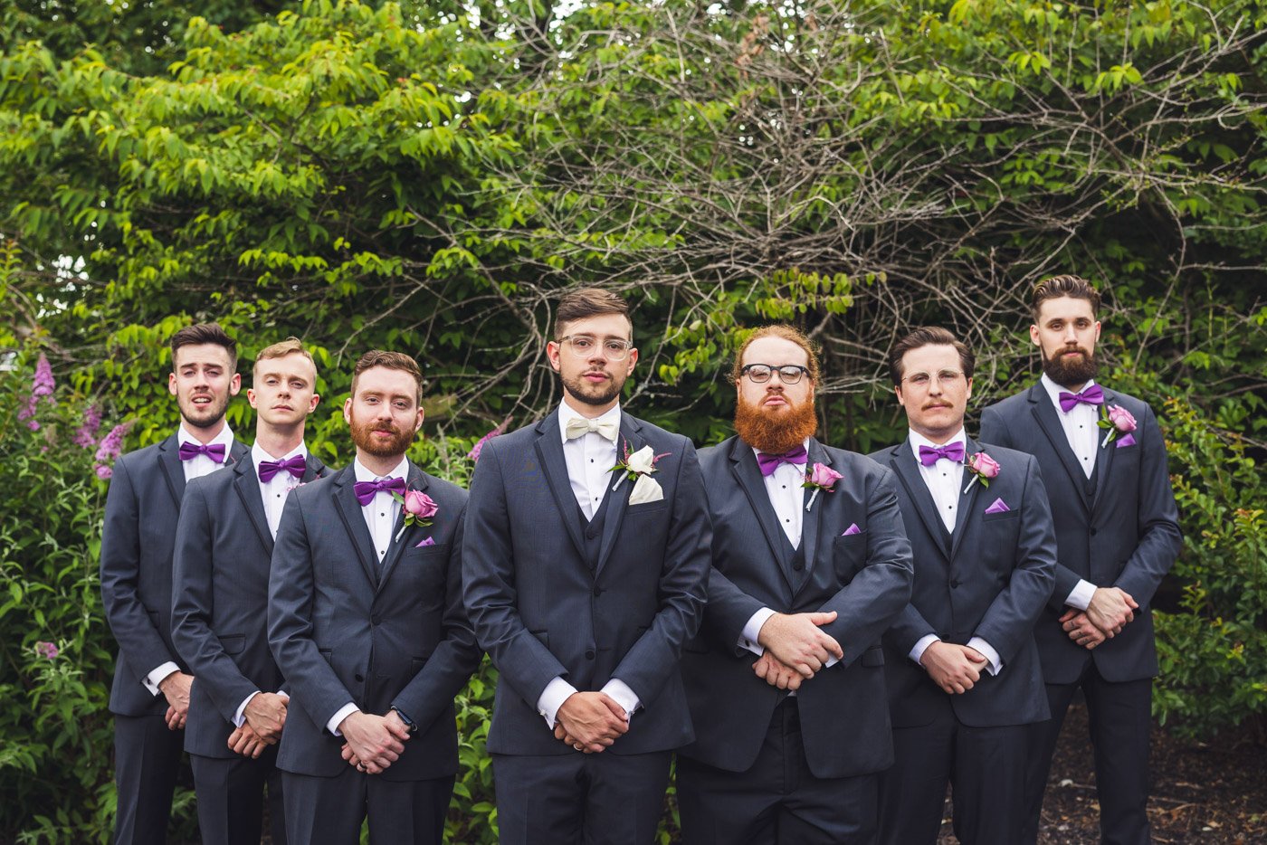 groomsmen lined up in flying v formation against greenery