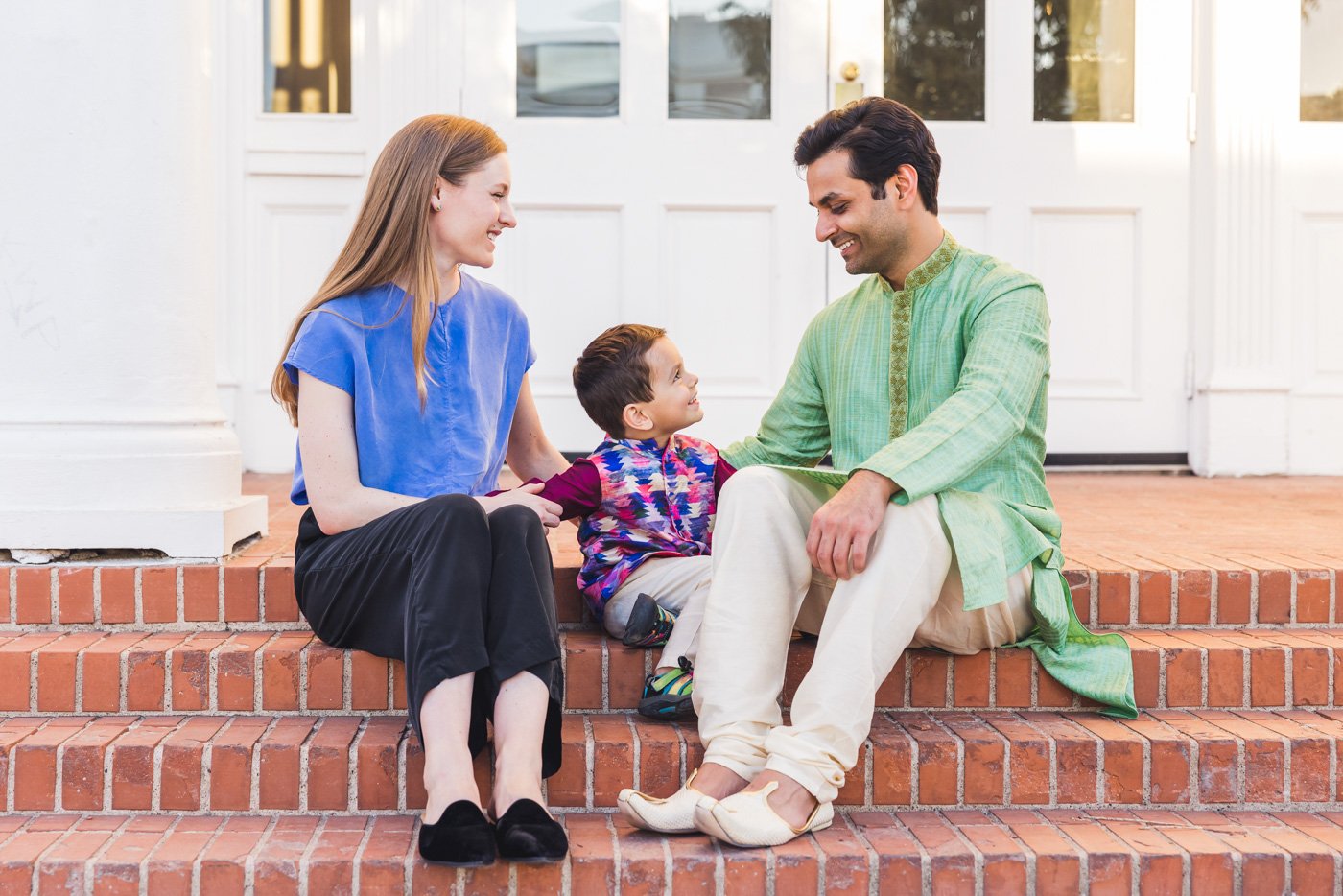 family sitting on red brick steps smiling and looking at each other