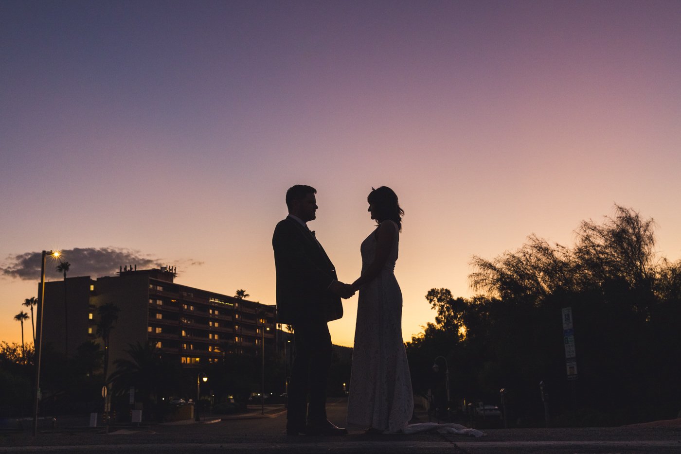 sunset silhouette of bride and groom in front of building and sky