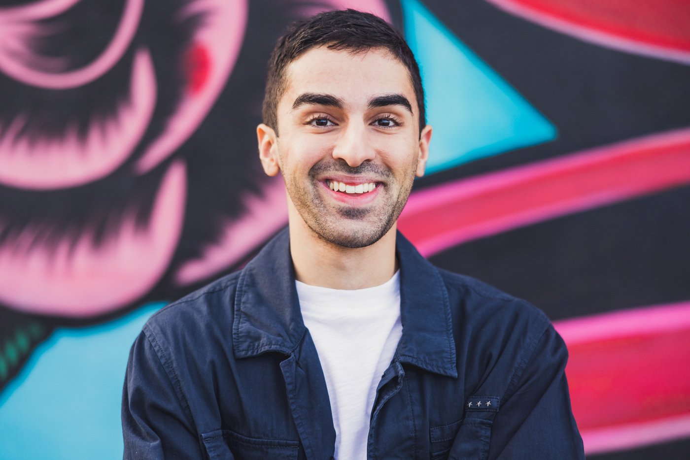 man smiling in front of colorful mural for headshot