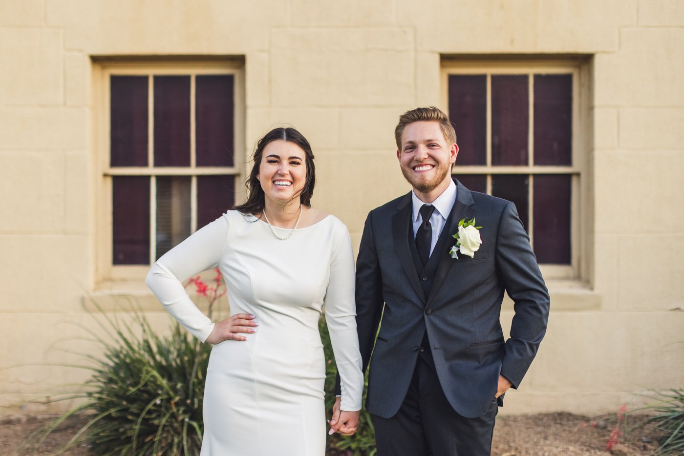 bride and groom laughing holdings hands in front of building