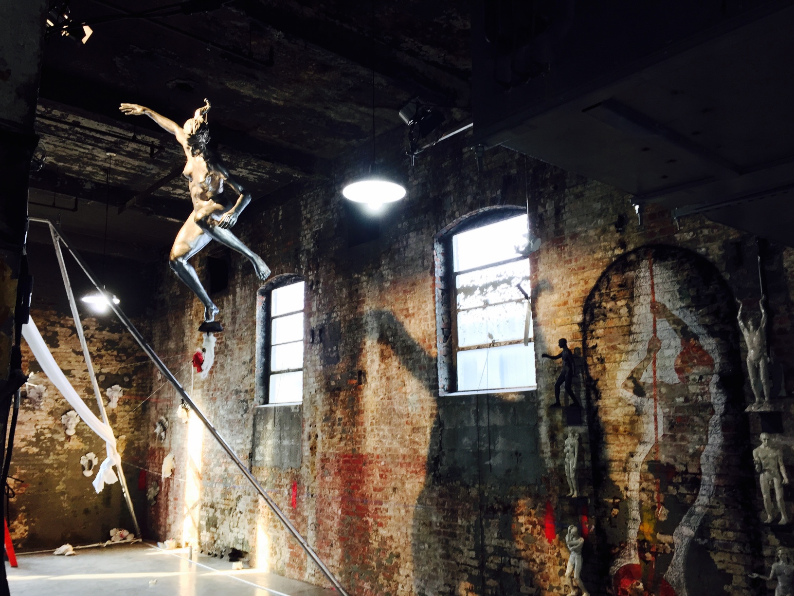 Installation view at Whispering Voices, in Greenpoint Brooklyn, of our collaborative art project of great interest to curators and arts institutions showing standing figure sculptures, bronze figures, ceramic figures and a hanging lifesize female nude figure sculpture (above) as well as wall-mounted head sculpture masks on the back wall.