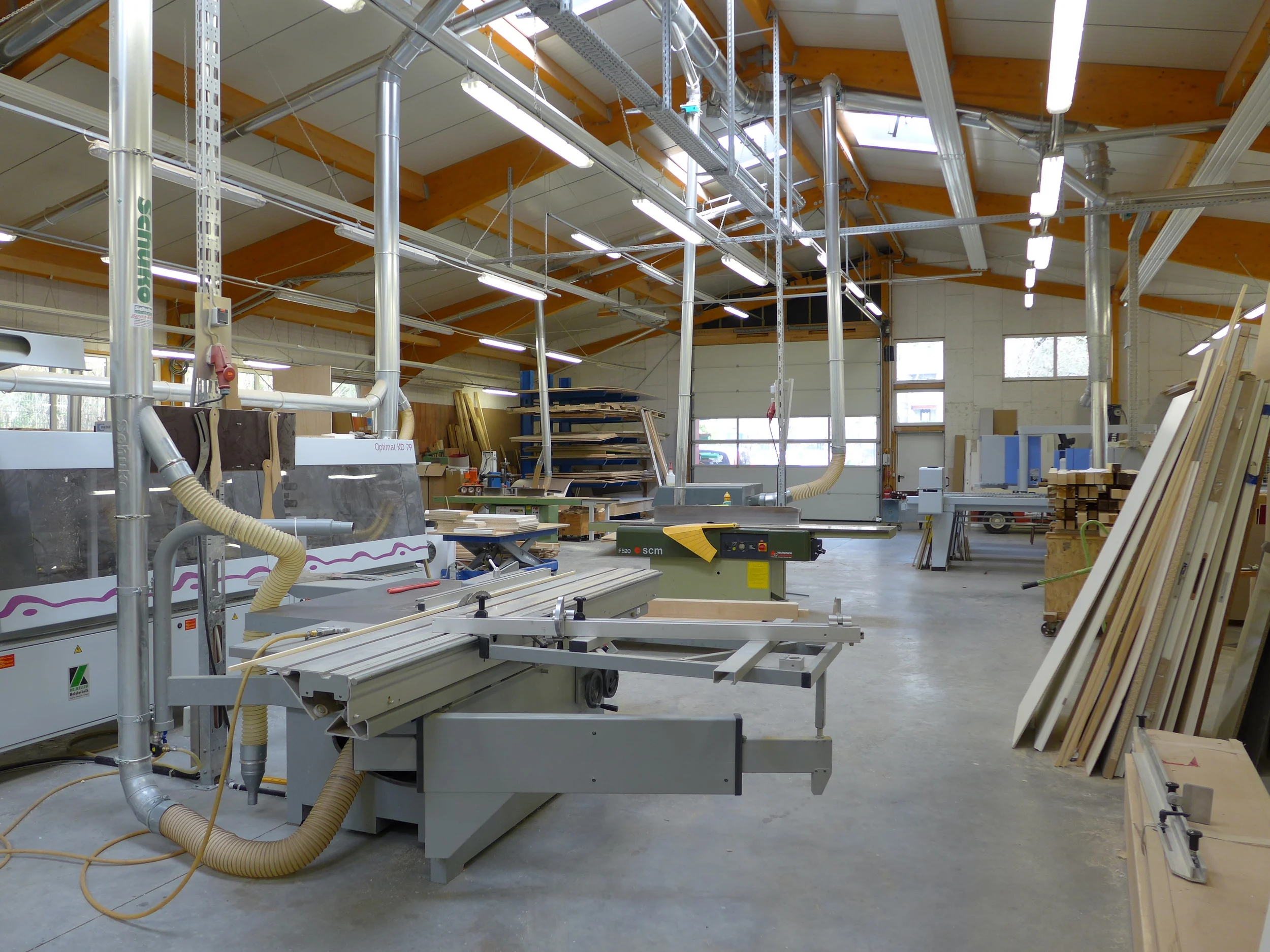Unsere weitläufige Produktionshalle ist mit modernsten Maschinen ausgestattet. Zum Maschinenpark gehören unter anderem eine NC-gesteuerte Plattensäge, ein CNC-Bearbeitungszentrum, eine Kantenanleimmaschine und eine Vakuumpresse für Formverleimungen.