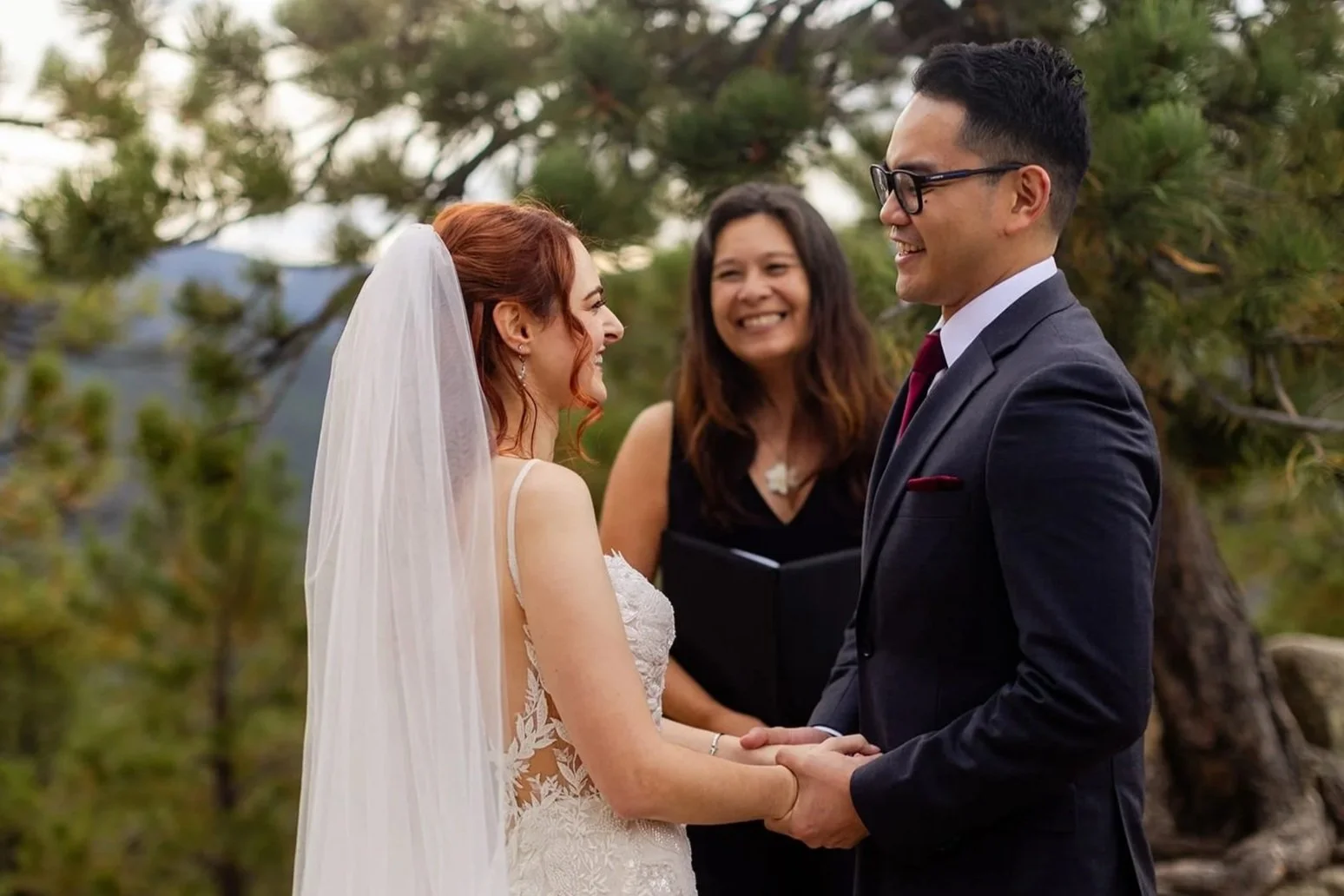An eloping couple smile and laugh during their ceremony while Officiant Lisa looks on smiling too.