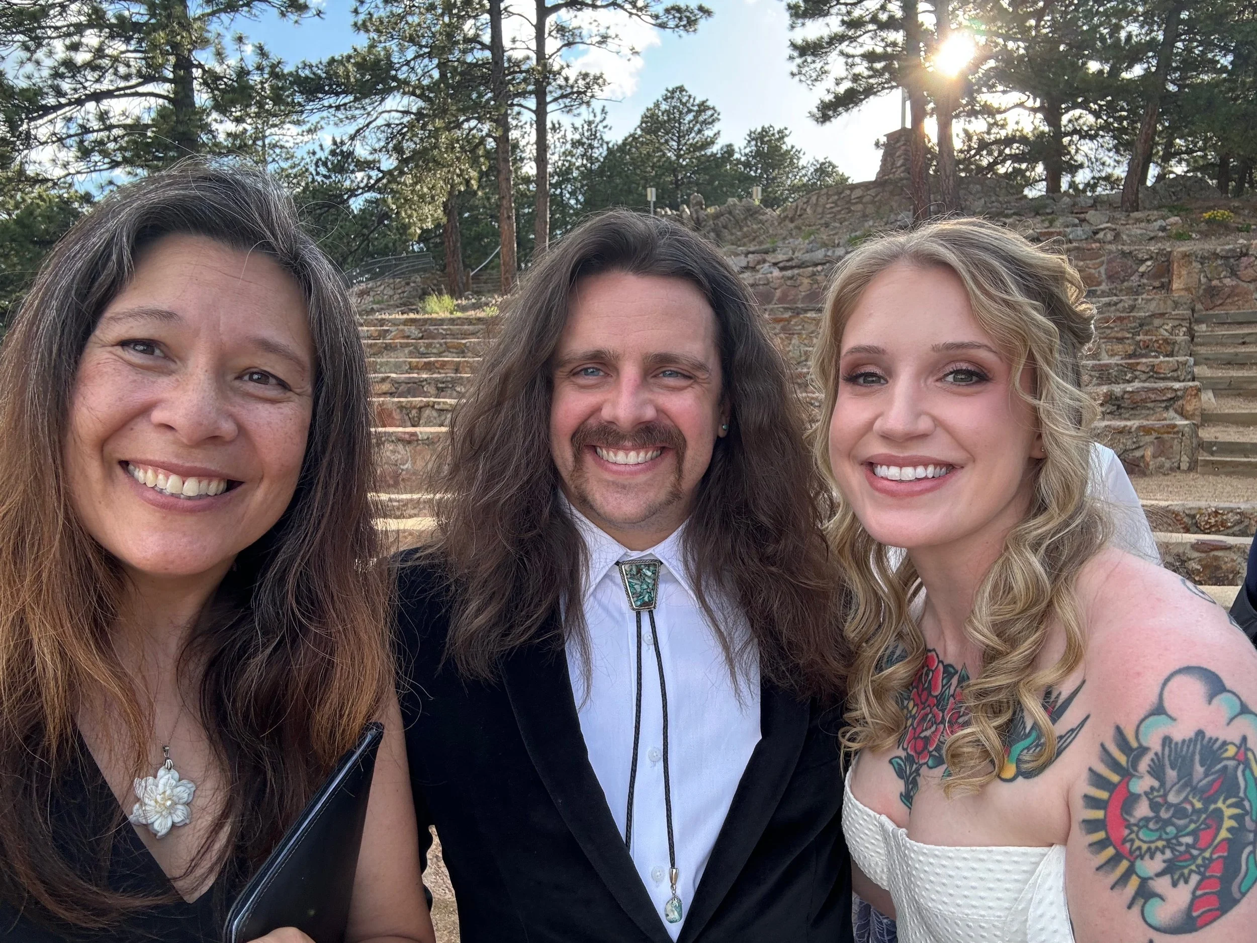 Officiant Lisa takes a selfie with Erin & Bobby with the amphitheater seating and sunset behind them.
