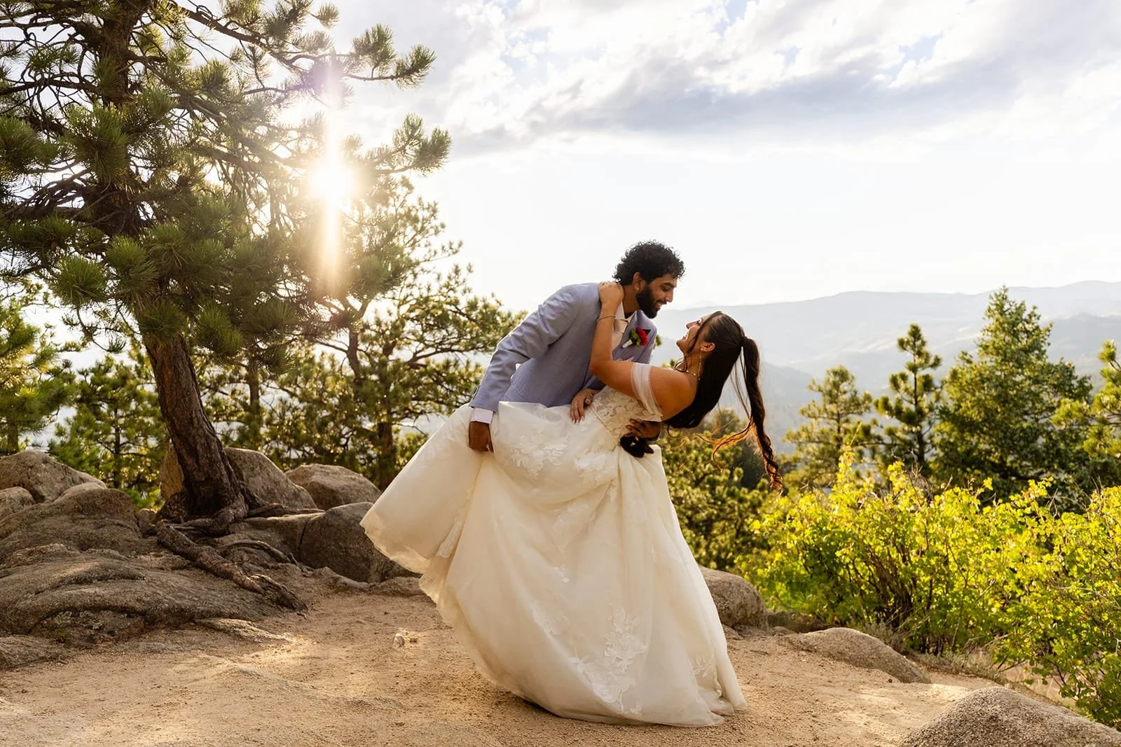A groom dips his bride in a dance movement with forest and mountain backdrop