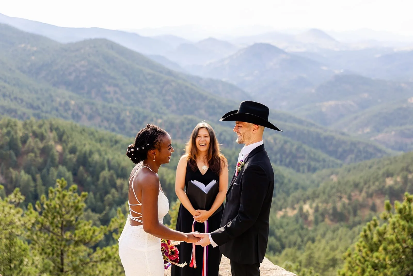 Officiant Lisa officiating an elopement ceremony with a groom with a cowboy hat and a rolling mountain backdrop.
