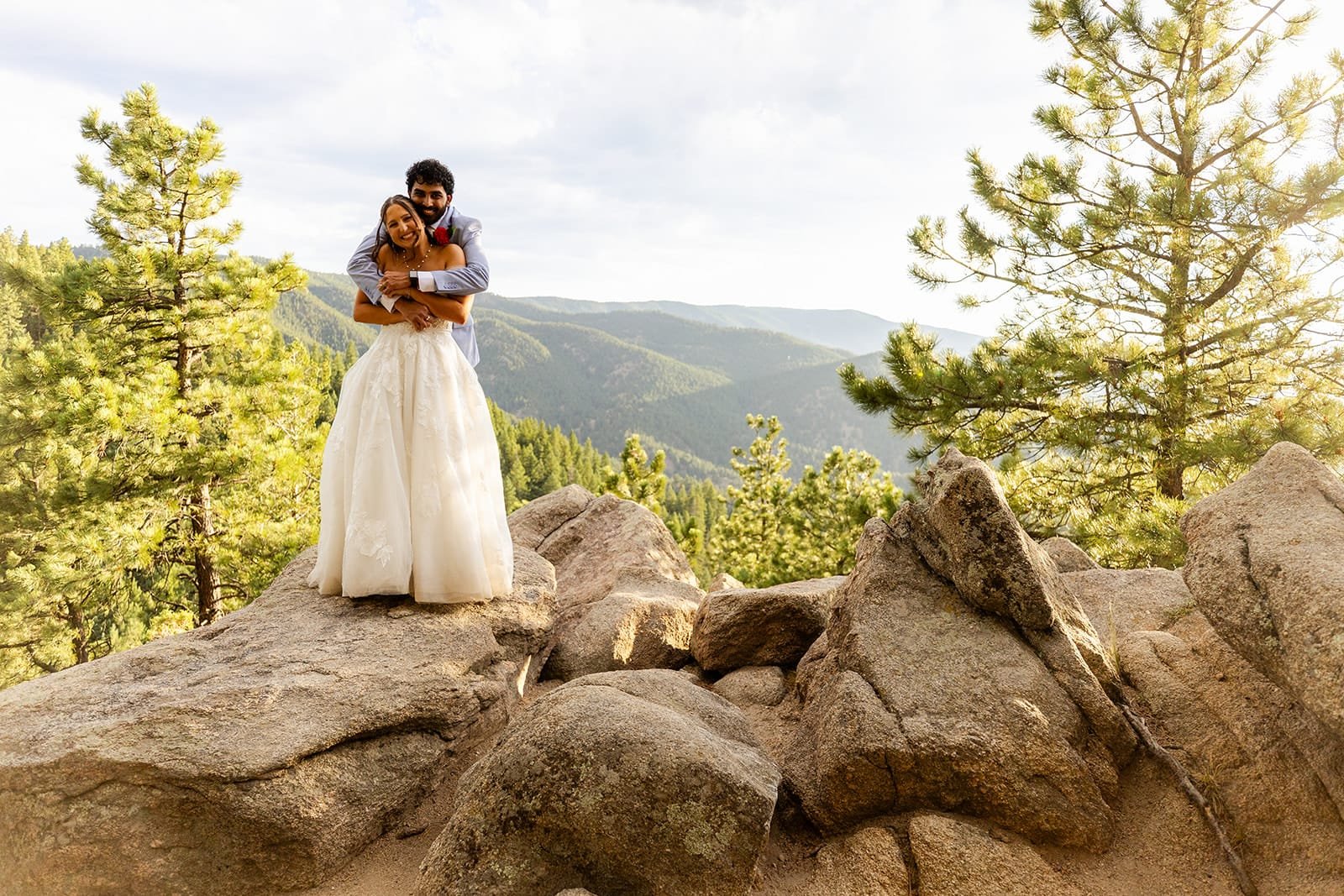 An eloping couple hugging on granite rocks with a forest and mountain backdrop
