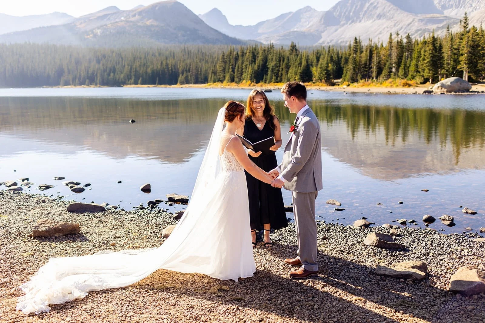 Officiant Lisa officiating an elopement ceremony for a bride and groom next to an alpine lake with a mountain peak backdrop.