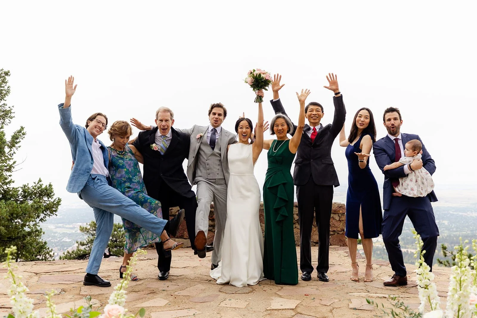 A just-married bride and groom celebrate in a group photo with their eight guests while all raise their hands or kick out their feet in celebration.