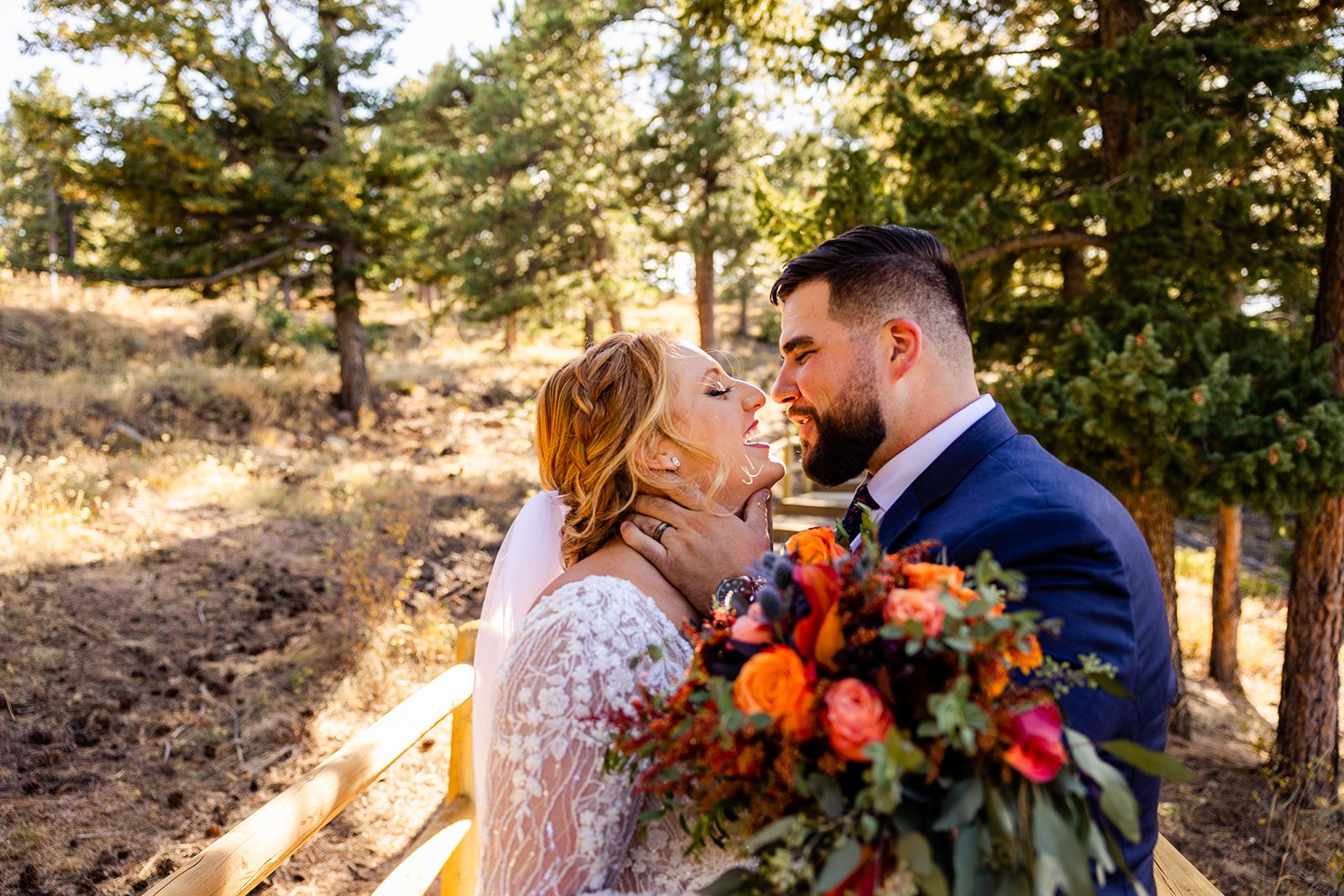A bride, with a bouquet of bright orange and red flowers, just about to receive a kiss from her groom.