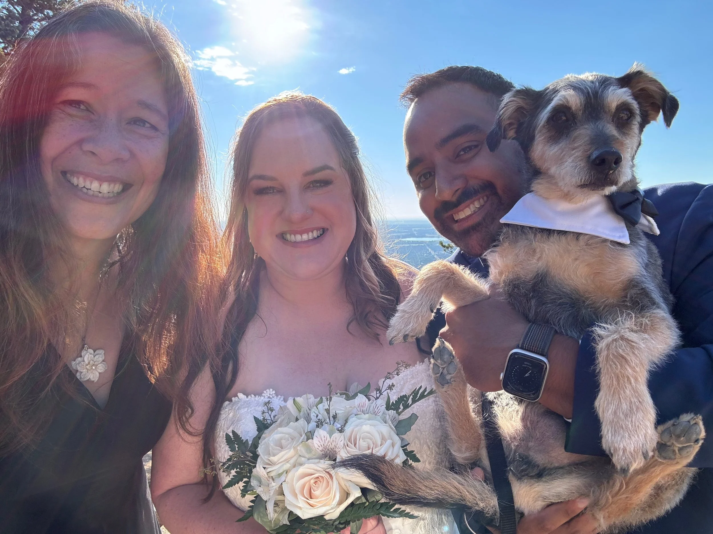 Officiant Lisa takes a smiling selfie with Stephanie, Eddie and their dog wearing a tuxedo outfit.