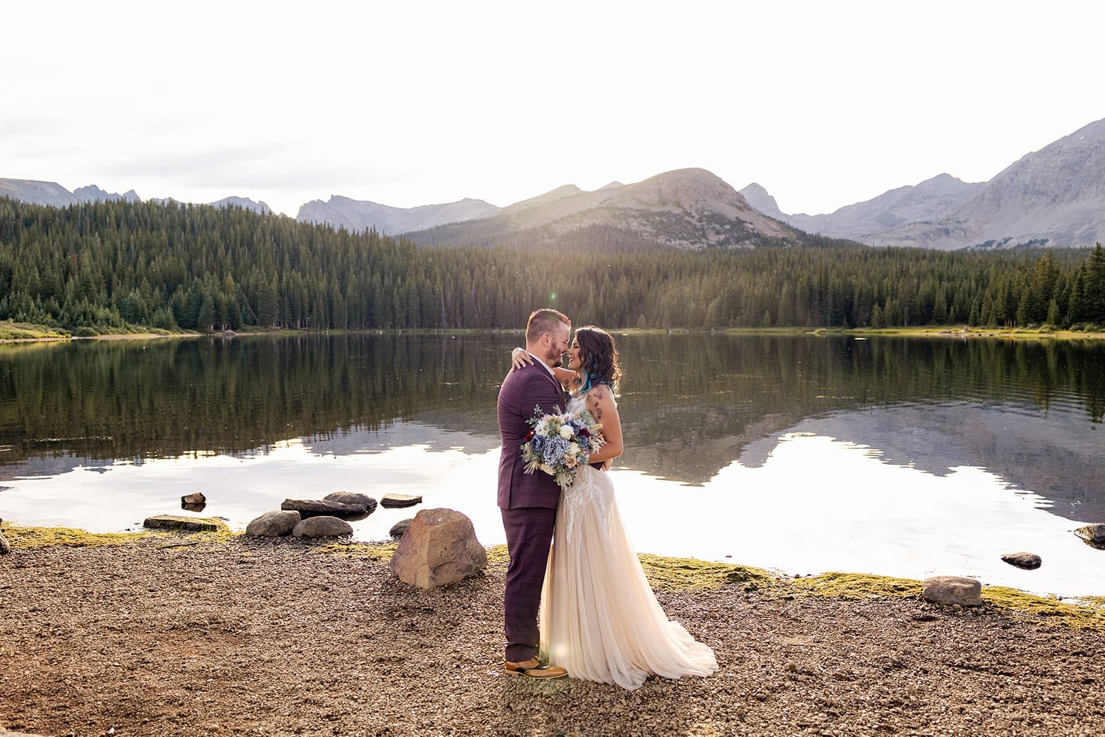 A newly-married couple about to kiss next to a lake.
