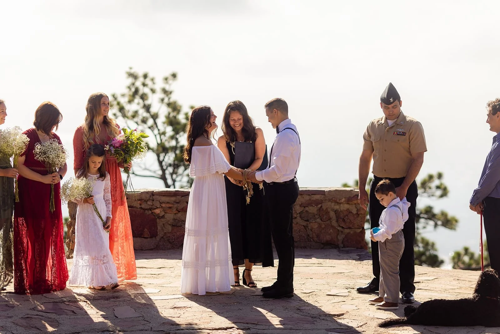 Officiant Lisa handfasts a bride and groom together during a ceremony in early morning light while their bridesmaids and groomsmen look on.