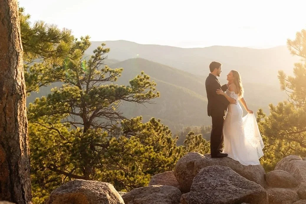 A just-married eloping couple dances on granite rocks with a mountain backdrop in soft sunset backlight