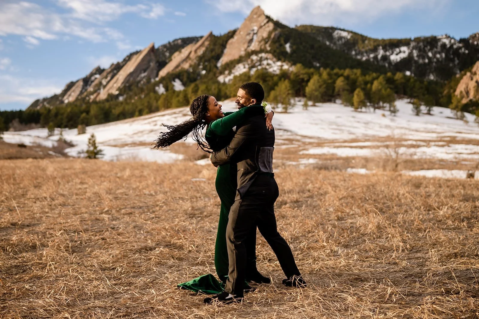 A groom gets ready to dip his bride in a dance move in a golden meadow with a snowy mountain backdrop.