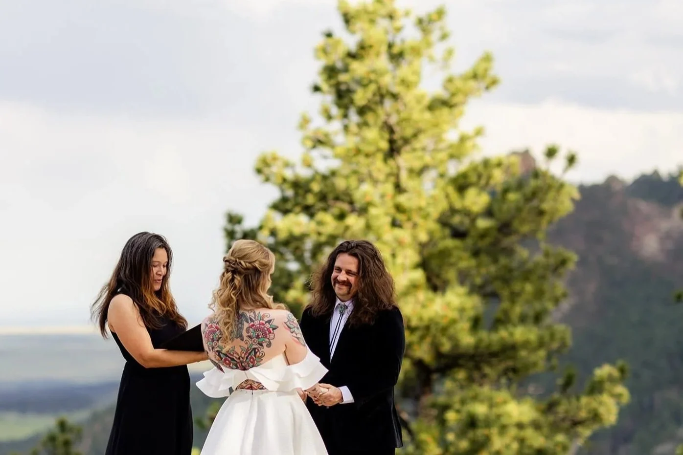 A bride & groom holding hands during the ceremony from an angle where we can see the groom's big smile.