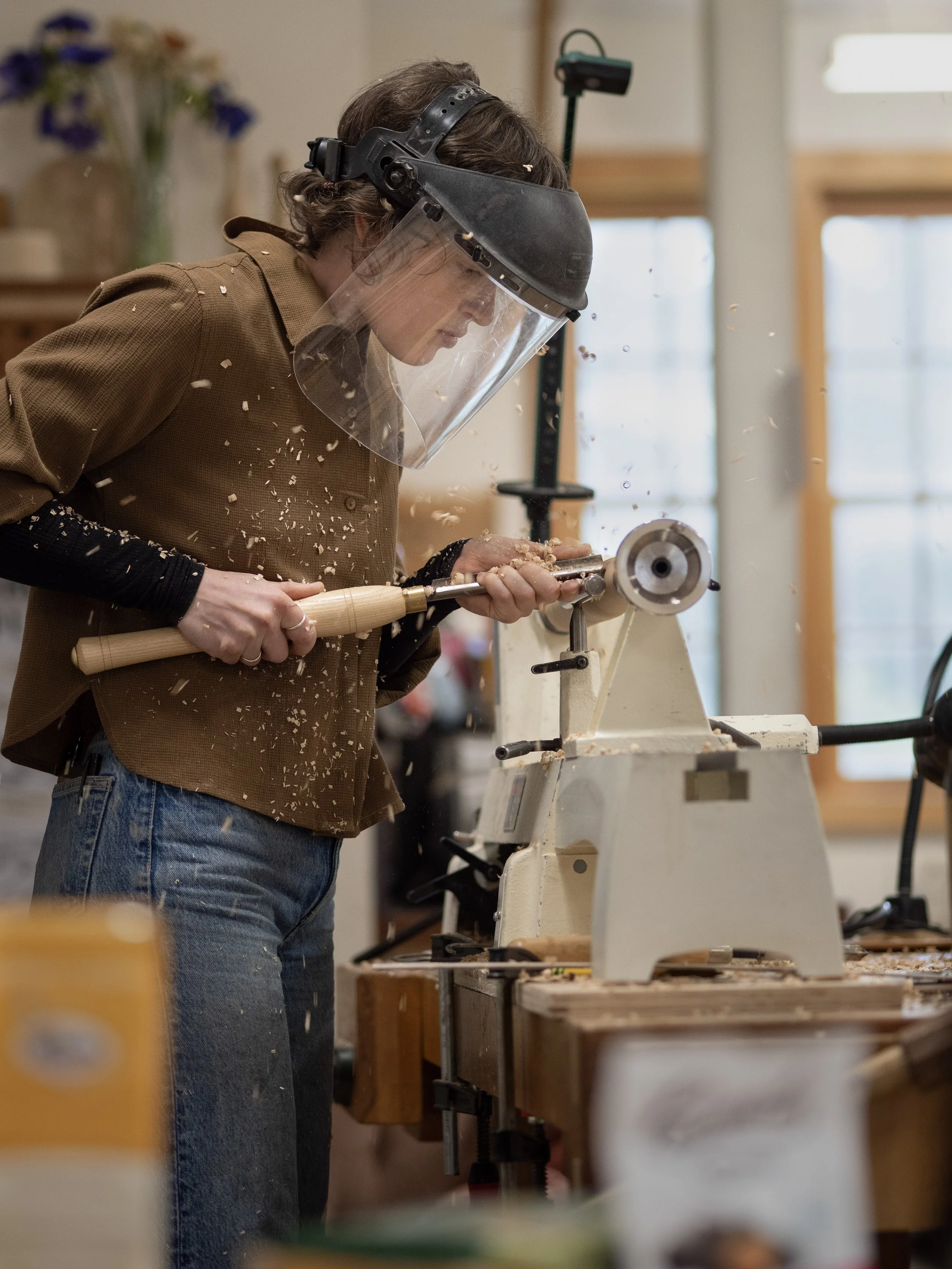A young woman using a chisel and a lathe doing woodturning.