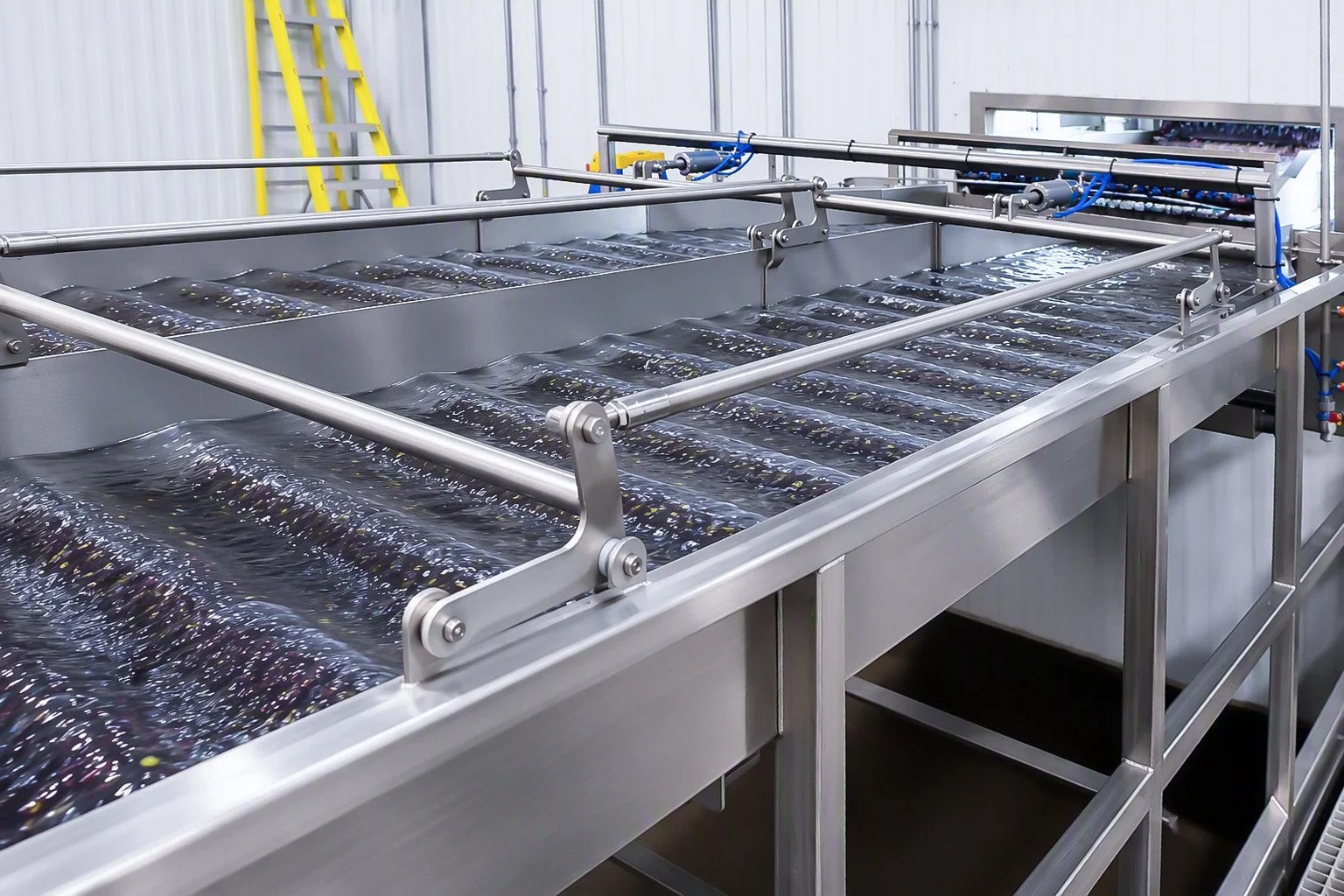 Close-up of a shaker with pipes, bolts, and a label, set in a warehouse or factory environment shaking strawberries.
