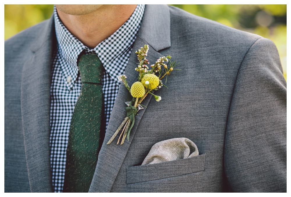 Wildflower boutonniere with yellow round flower on grey suit.