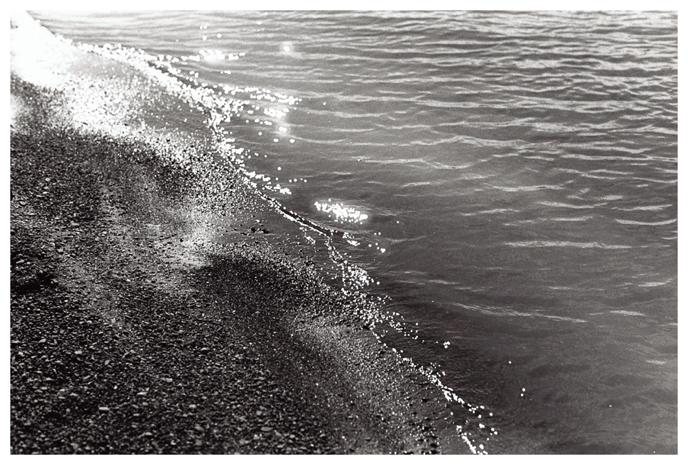 Sun sparkles on the waves of lake Ontario as they come to shore on the pebbles of the Scarborough Bluffs beach. 