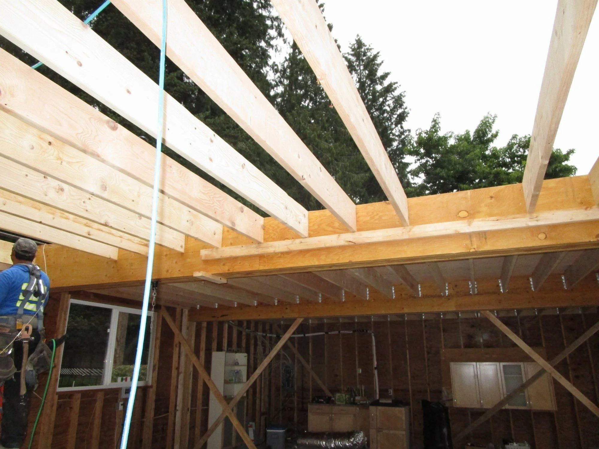 Framers hanging the new second floor joists in the final garage bay. Plywood flooring already installed in the far two garage bays.