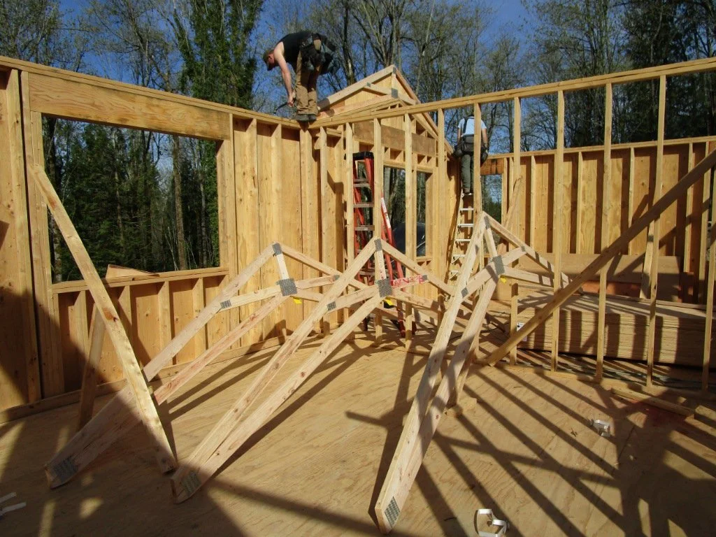 Turning right and looking through the future kitchen. Guys are laying up scissor trusses over the Master Bedroom. Scissor trusses have a sloped bottom chord.