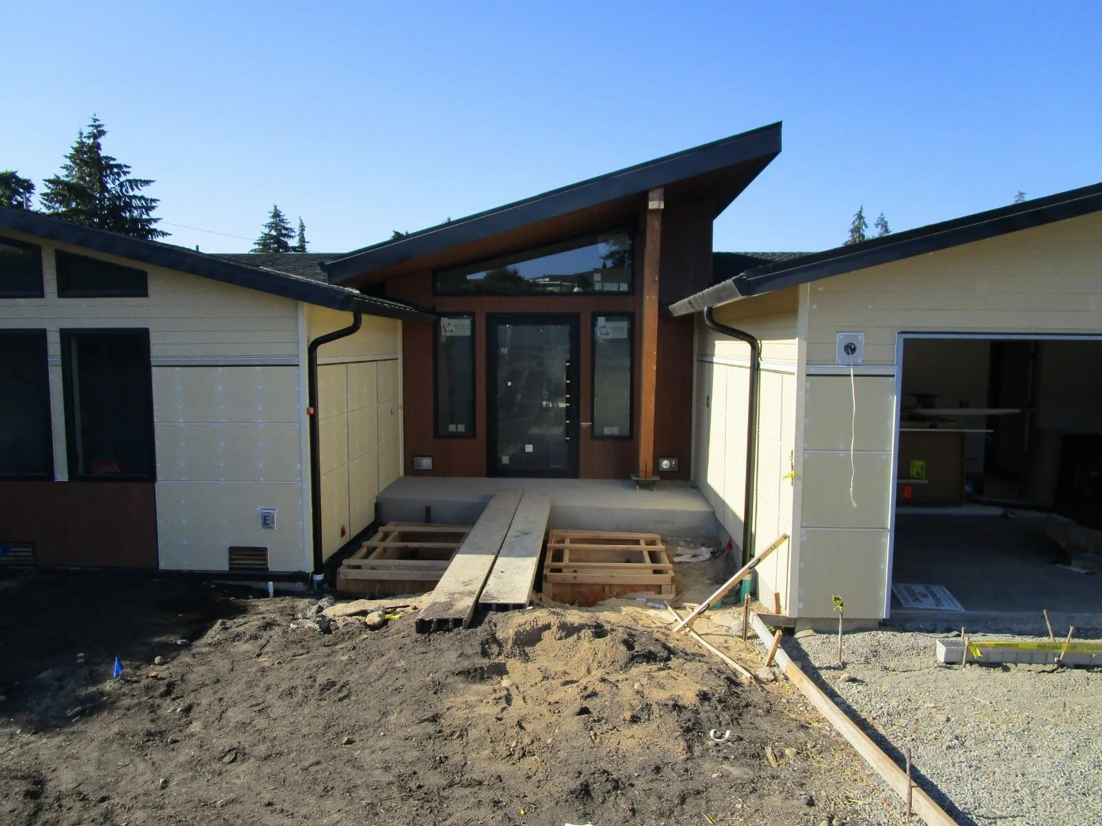 On either side of a boardwalk are forms for a pair of reflecting water pools. Exterior paint should happen soon.