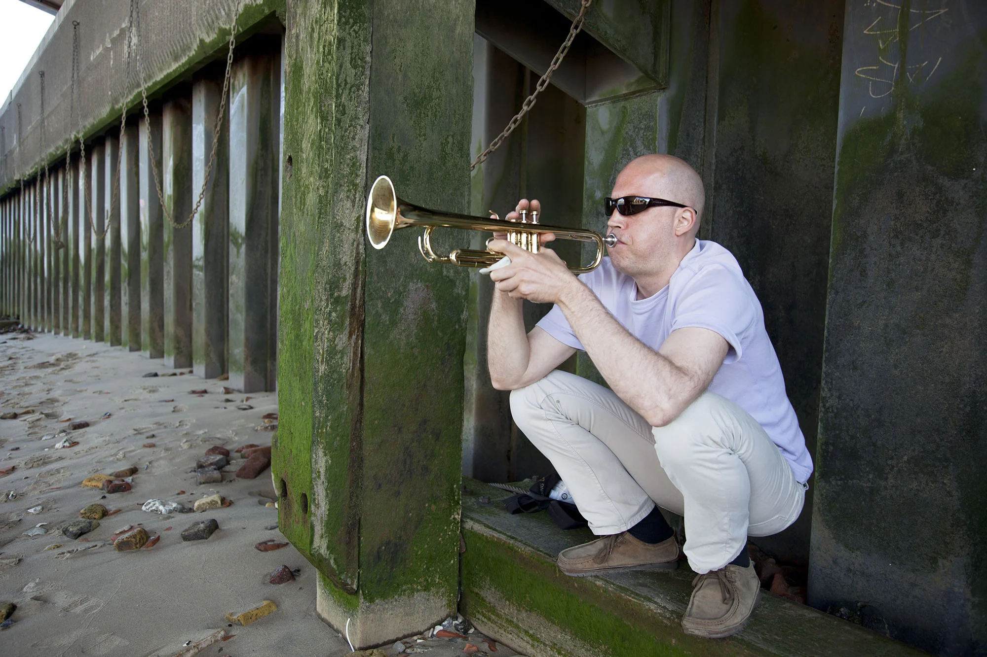 Man plays a trumpet underneath Blackfriars Bridge on the shore of the River Thames.