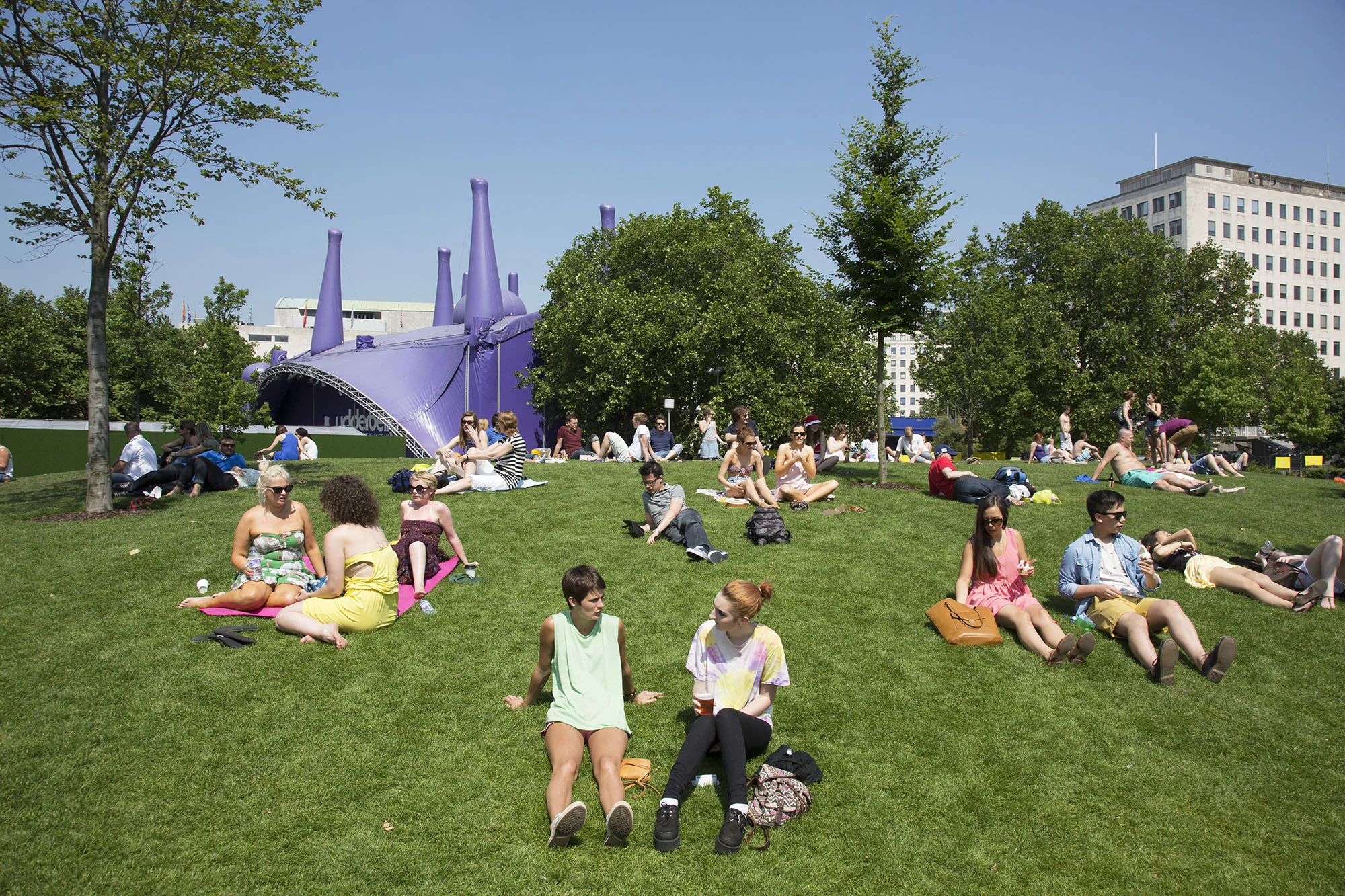 People gather on the grass in the sunshine at Jubillee Gardens on the South Bank.