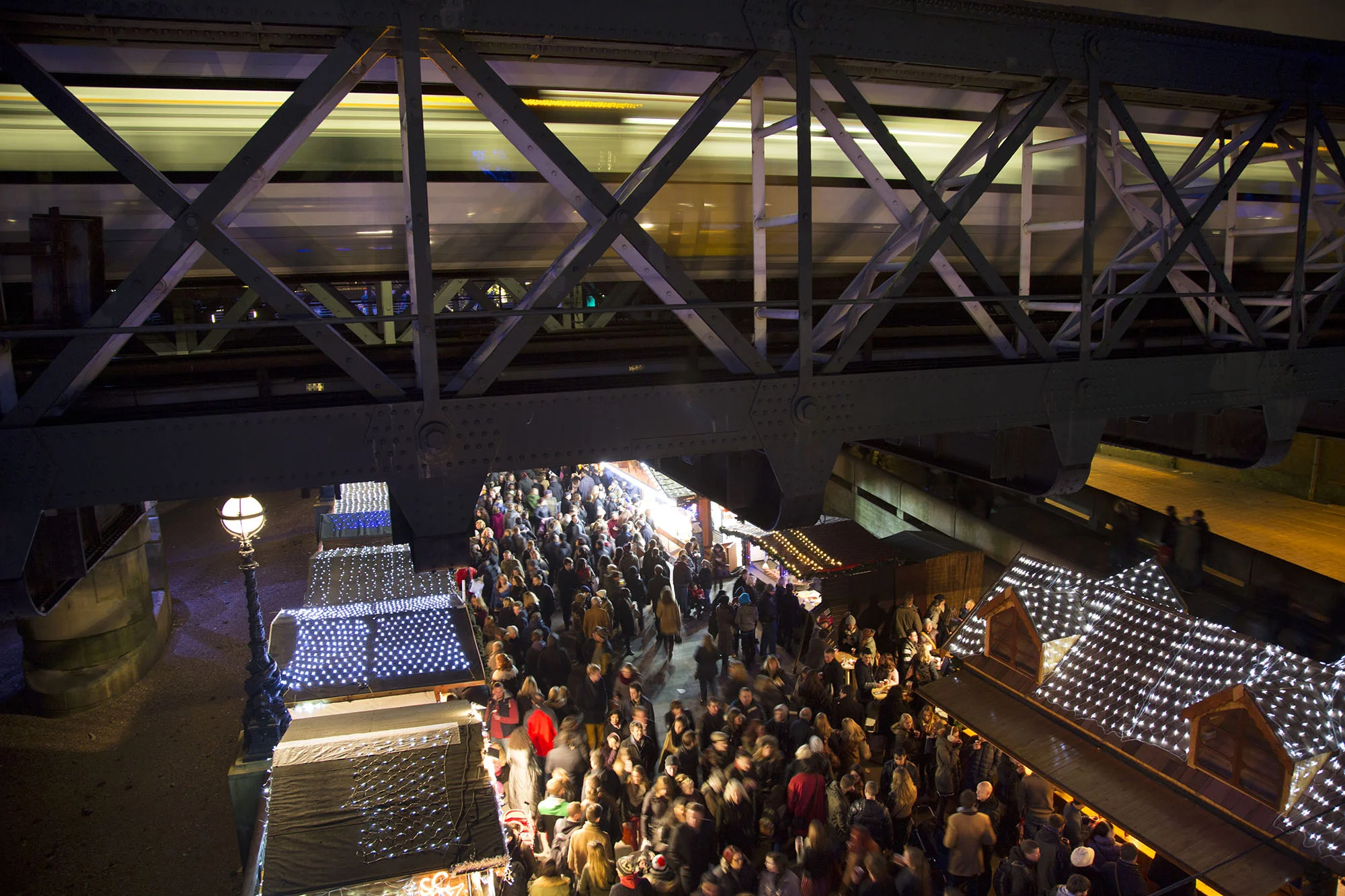 Huge crowds gather at the Christmas market along as a train passes over Hungerford Bridge.