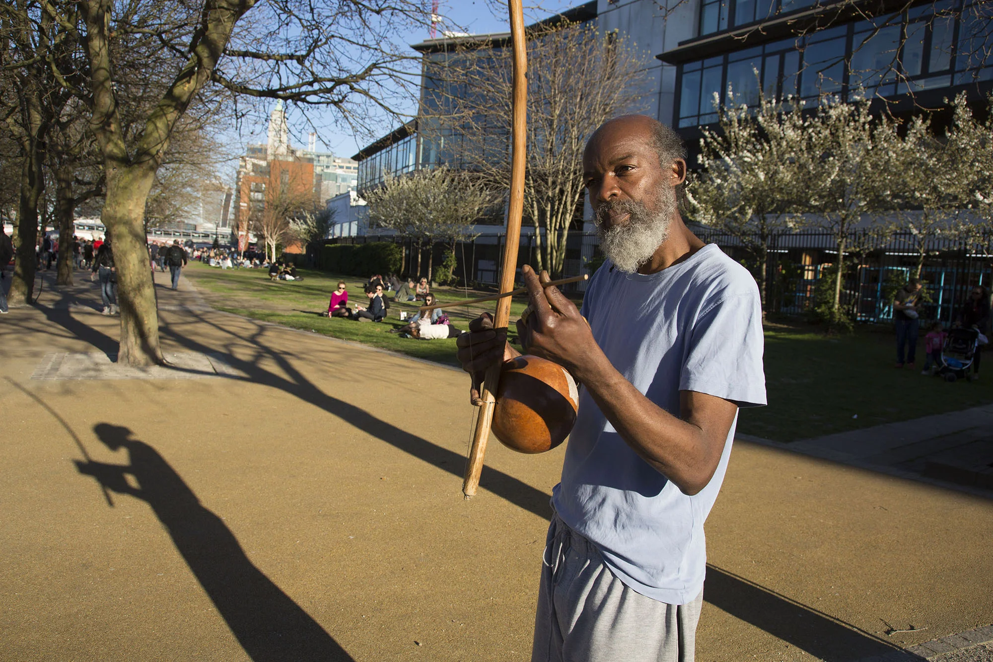 Busker casting his shadow in evening light playing a berimbau.