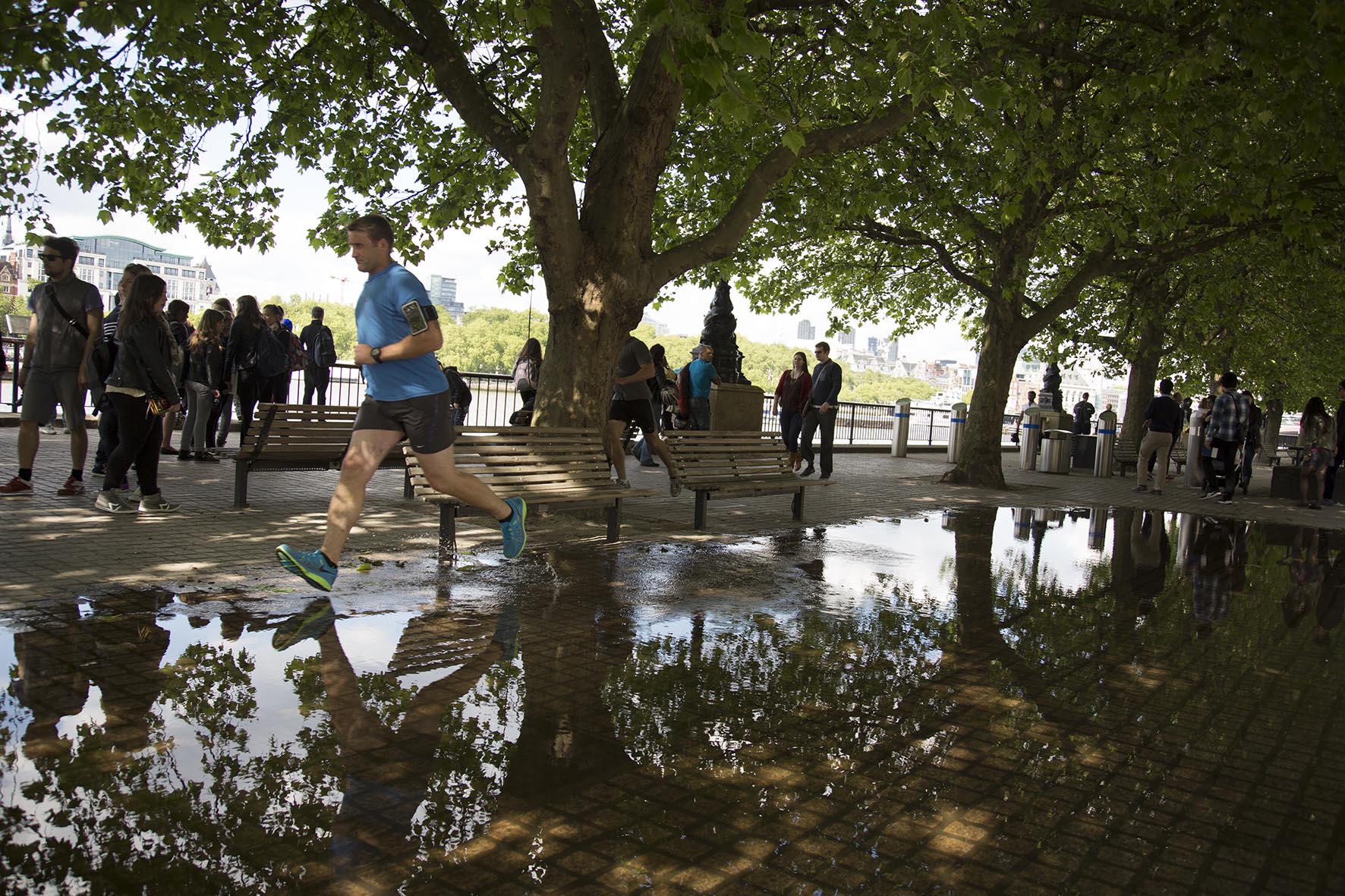 Man running through a large puddle on the riverside walkway.