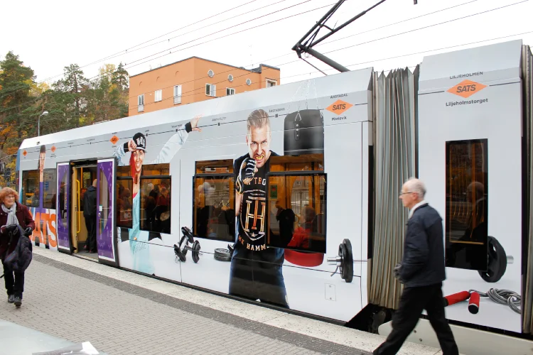 2 tvärbanetåg med kampanjbilder för SATS Sverige