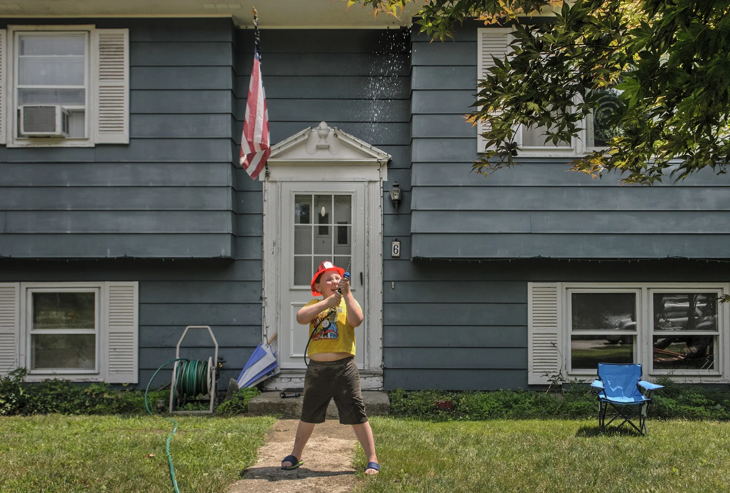 07.09.2014 - Windham, Ct. - Equipped with a toy fire hose and water-filled canisters strapped to his back, Mason Varga, 6, stands in his front yard spraying water on a pretend fire in his "climbing tree." Mason was home with his father, Stephen Varga, a paramedic and Windham Center volunteer firefighter. Mason says that when he grows up he wants to be a Connecticut firefighter for six-months out of the year and a State Trooper in Alaska for the other six. "They help out their state," he explained, "And in the winter, guess what?...they go out in snowmobiles."