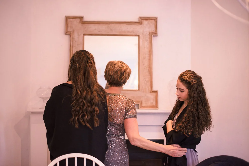 Mother of the bride and junior bridesmaids get ready in front of mirror
