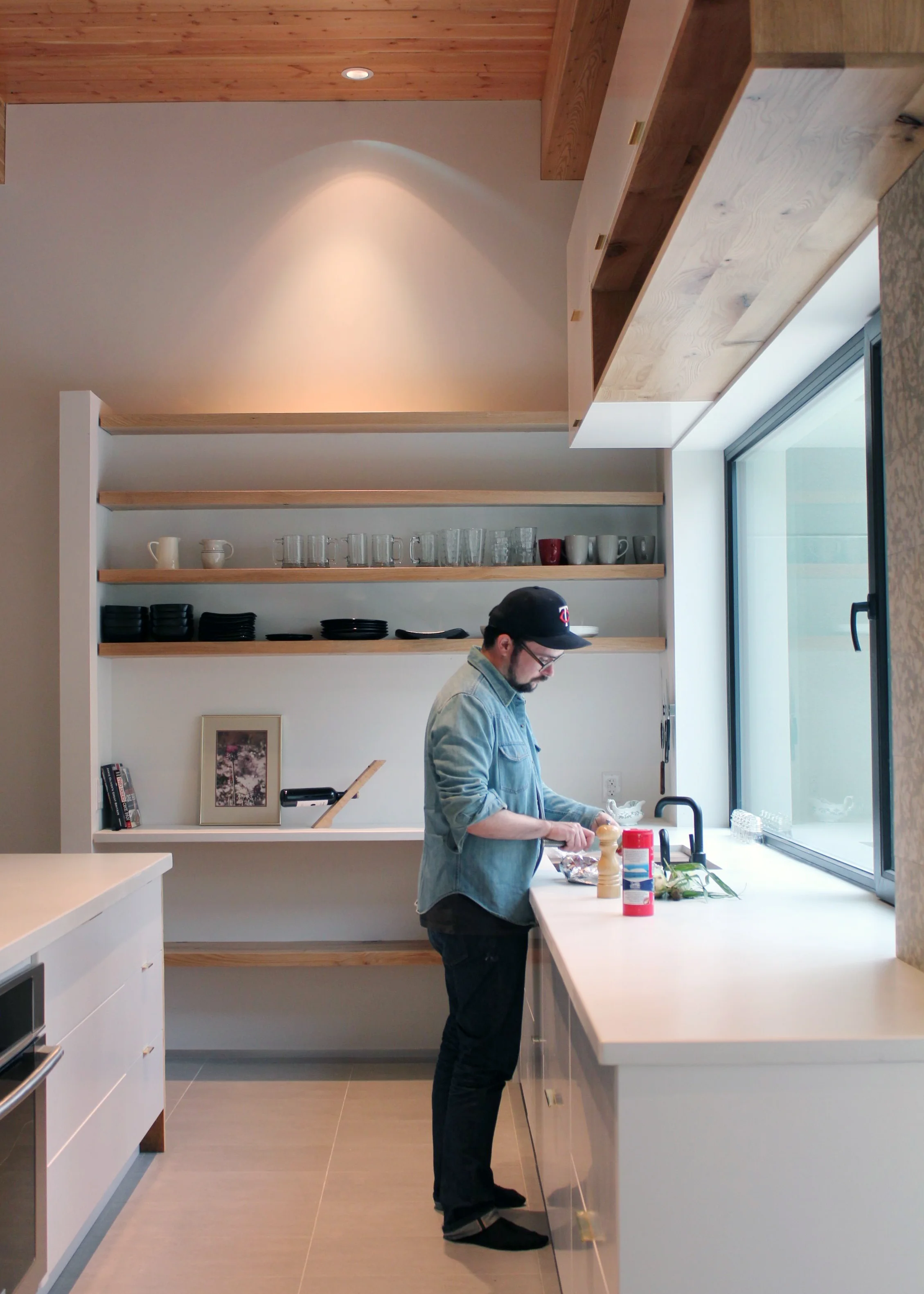 kitchen view with solid wood open shelving, brass drawer pulls and white concrete counter tops