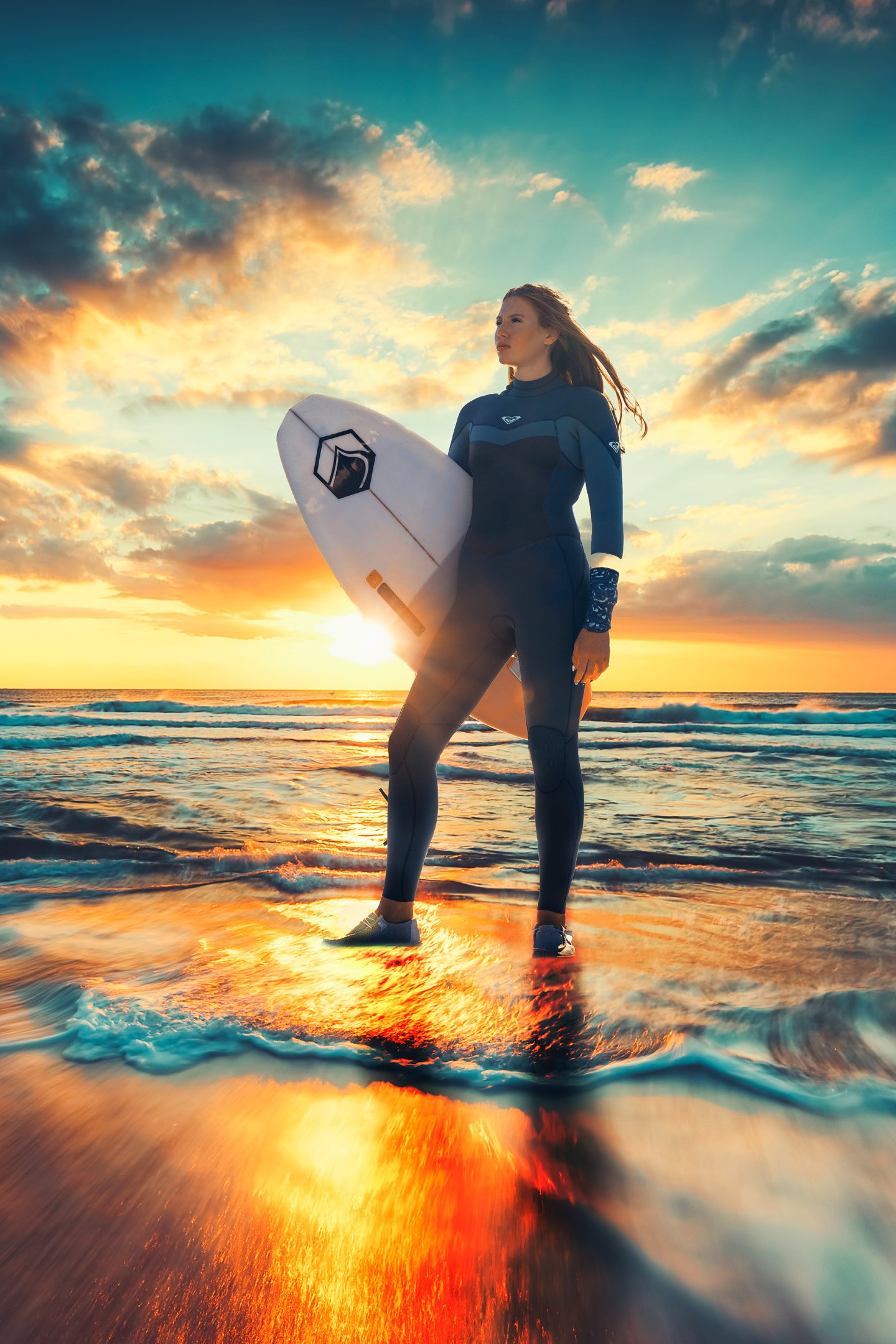 Surfer girl emerging from water on shore holding surfboard with blue skies and sun shining 