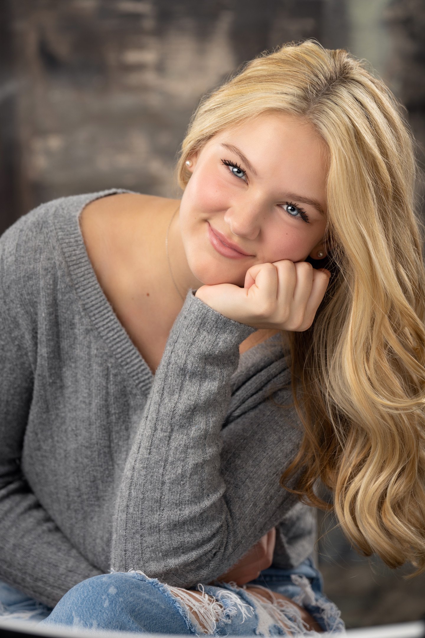 close-up portrait of girl with grey sweater and a soft smile leaning onto hand rested on leg