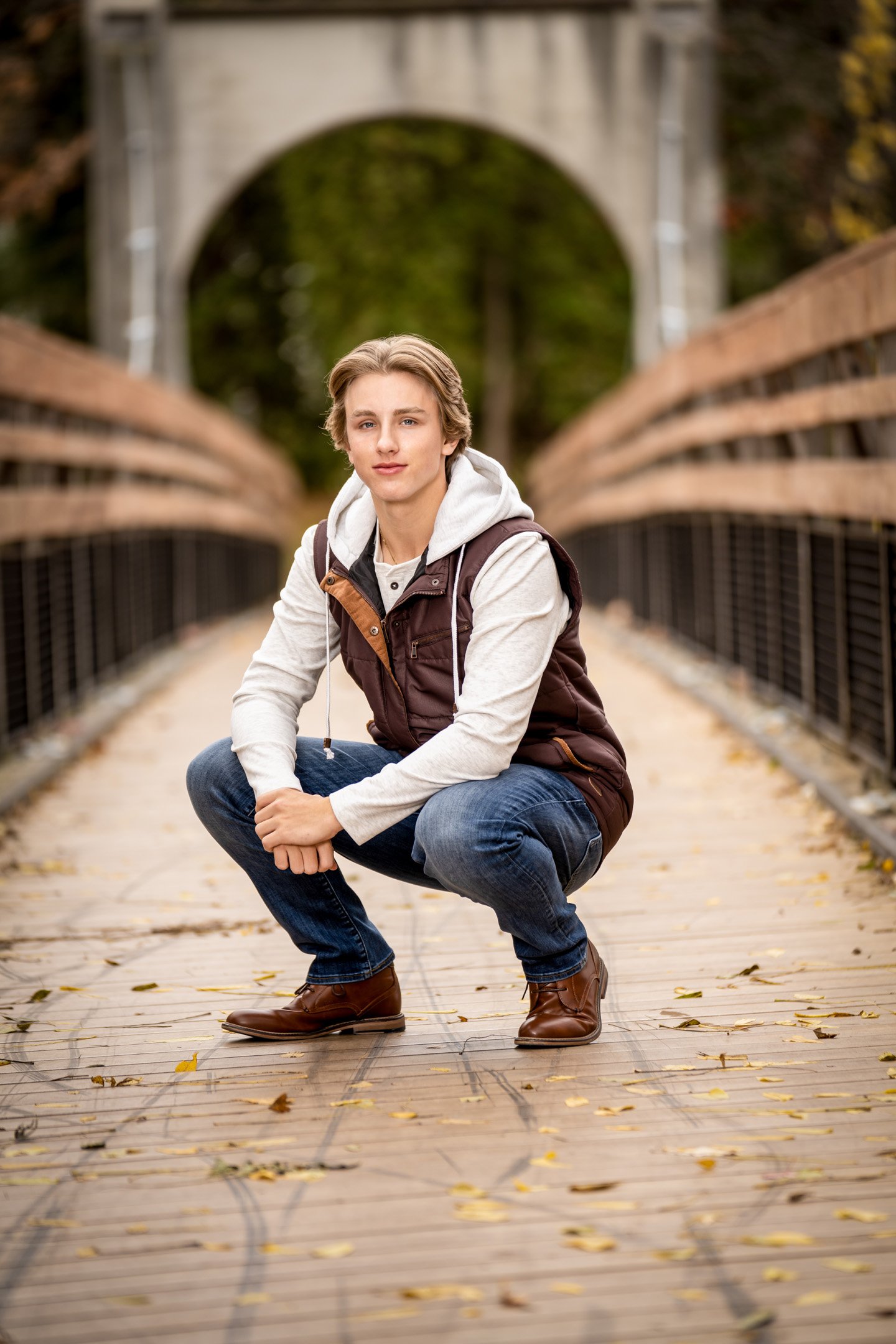 Kneeling down on bridge in fall weather senior boy portrait