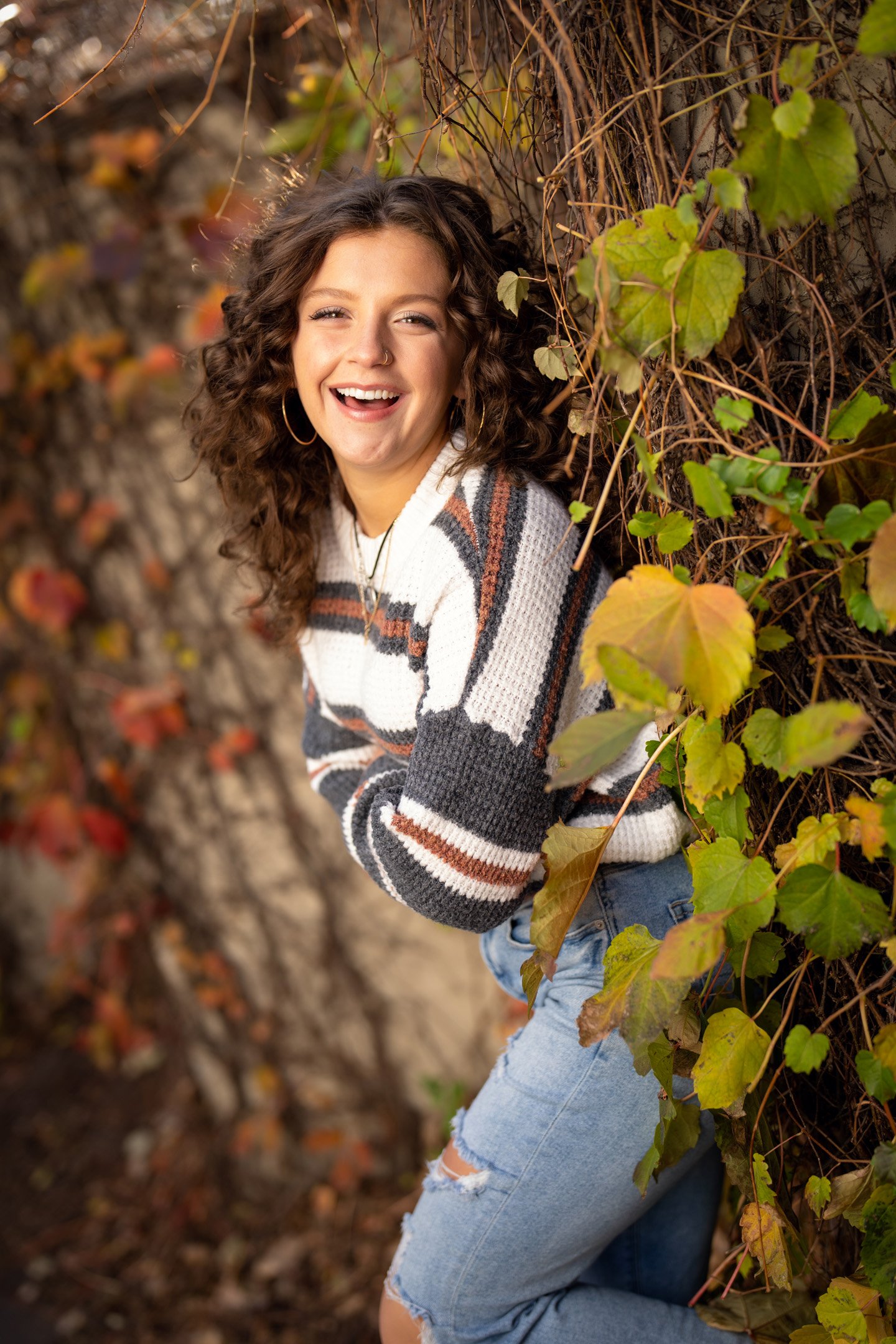 laughing girl in fall attire leaning against wall full of vines