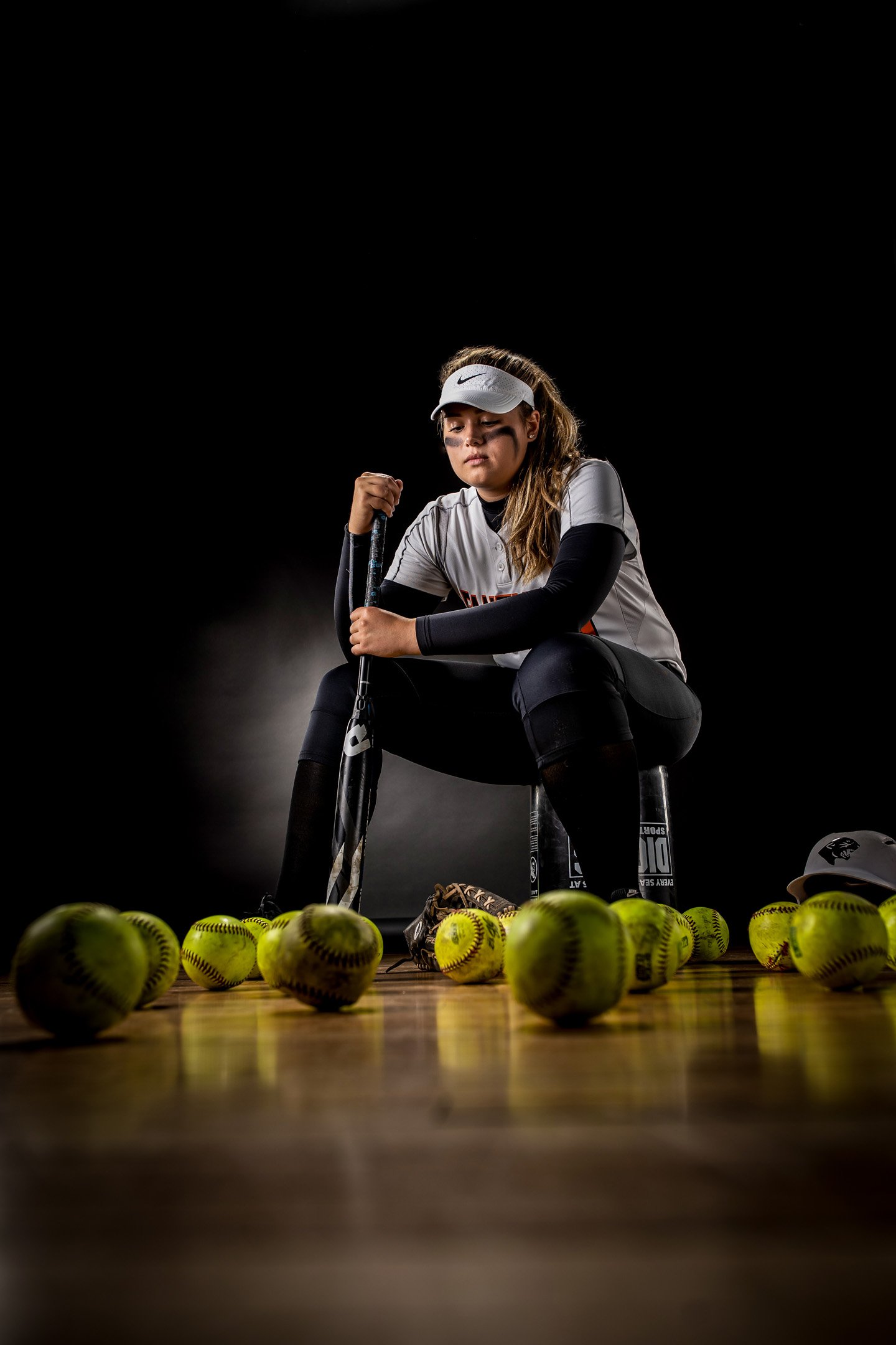 Softball player edgy in studio in uniform surrounded by softballs