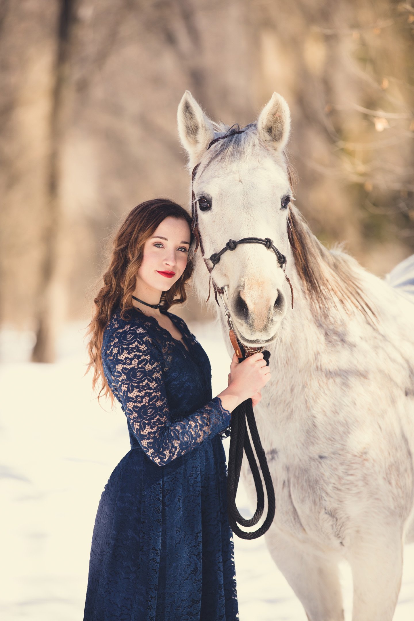 White horse in snow snuggled up to a girl in a navy blue dress posing for portrait