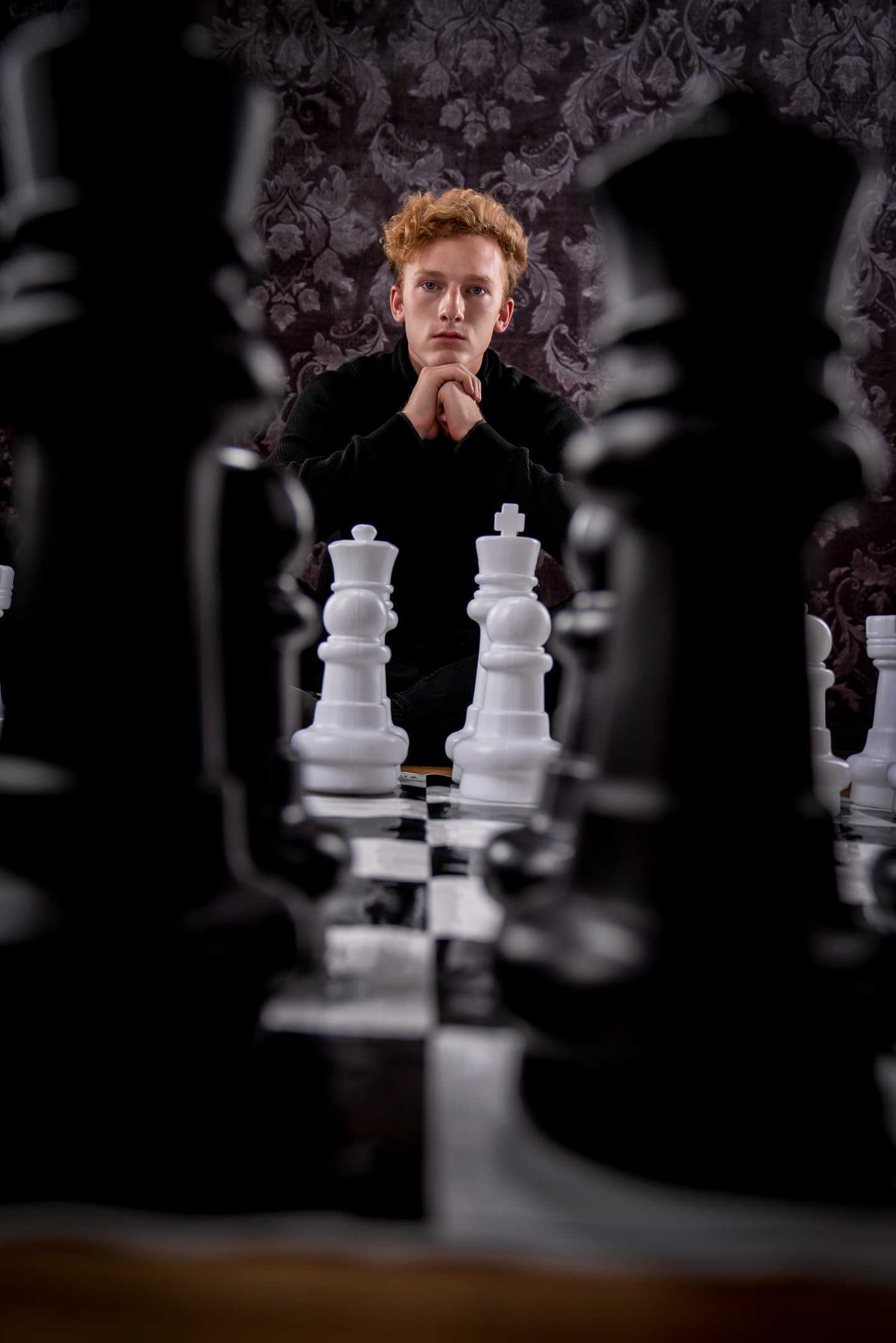 Looking through from a low angle of chess pieces of a boy playing chess