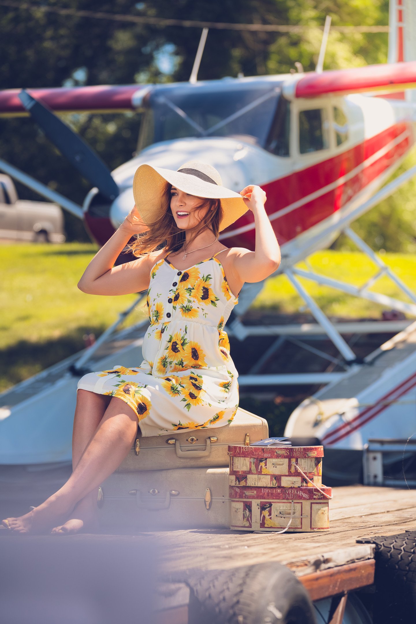 Seaplane set at dock with girl sitting on suitcases in sunflower dress and hat