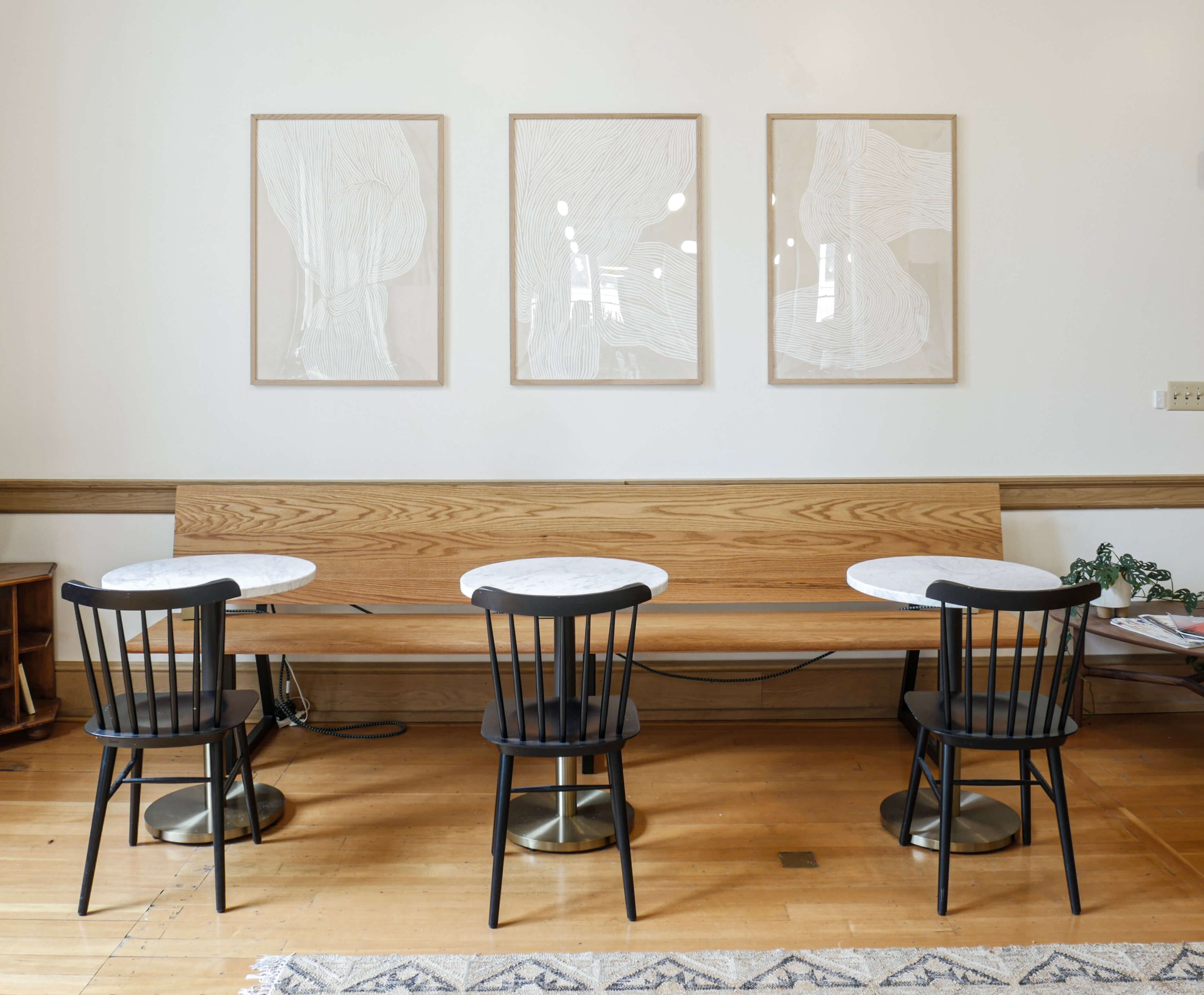  three marble bistro tables, three black salt and pepper chairs and an oak banquette 