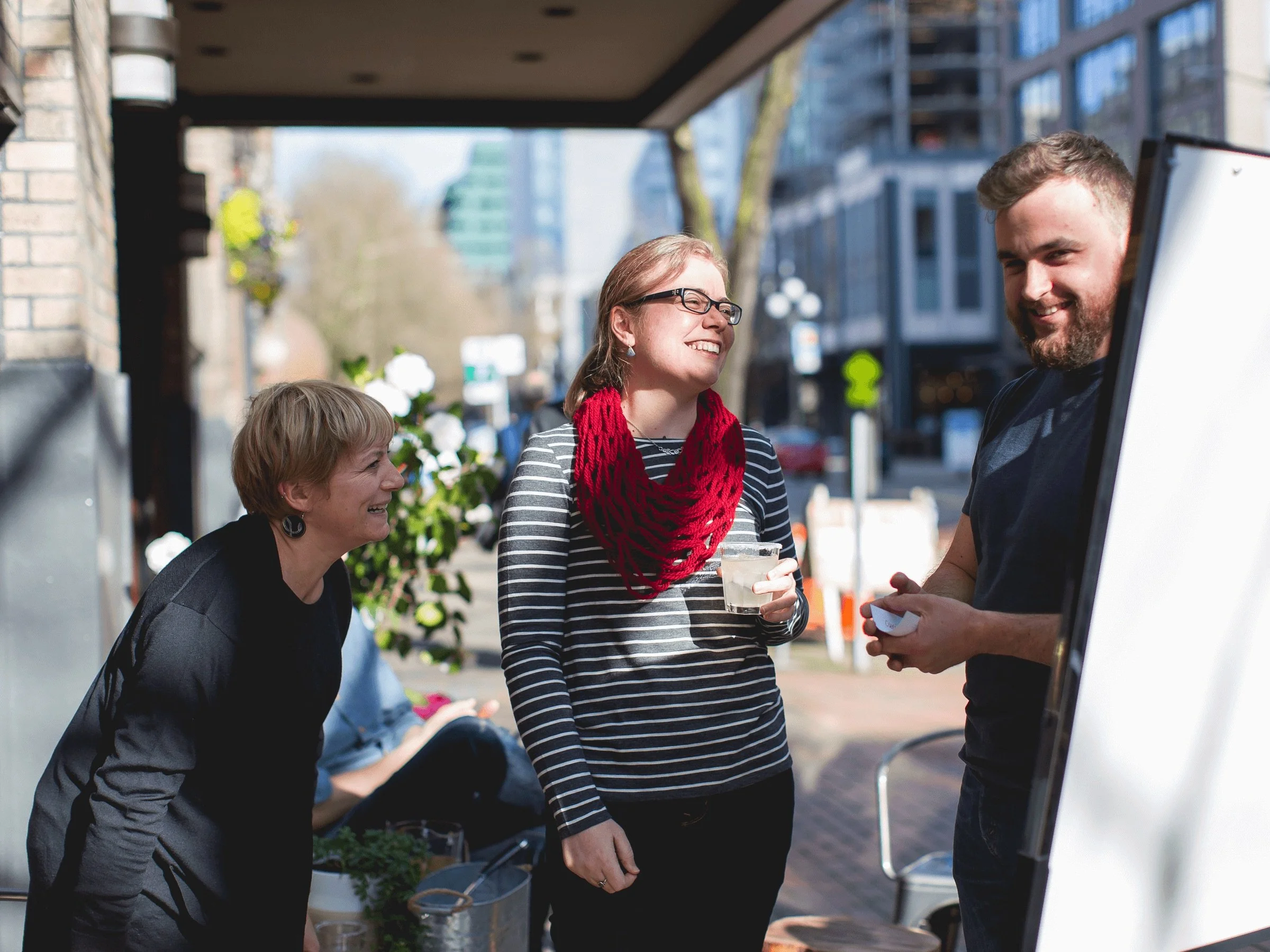 Two women and a man enjoy a sunny outdoor happy hour