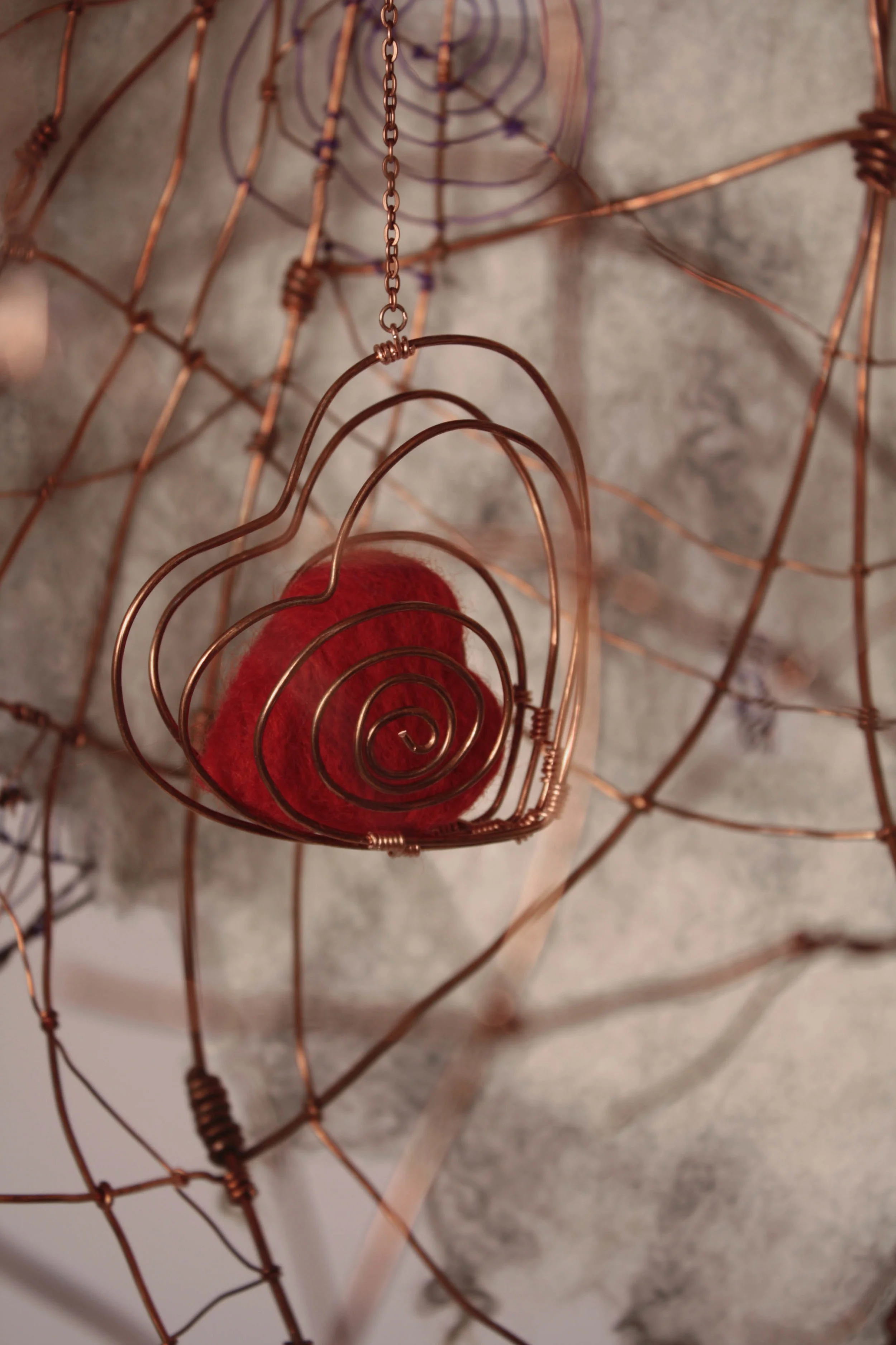 3D felted red heart inside a copper wire heart-shaped cage dangles inside