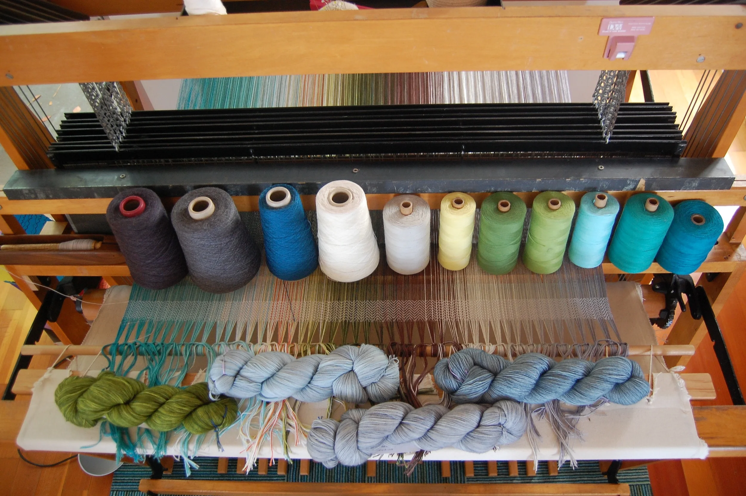 Some weft choices. From left: the superwash wool in midnight, steel, lapis and ecru; the cotton in EC cloud grey, light yellow, dark green, light green, EC sea foam, EC blue-green, peacock; MadTosh superwash lace in Jade, Mica, Aura, Well Water.