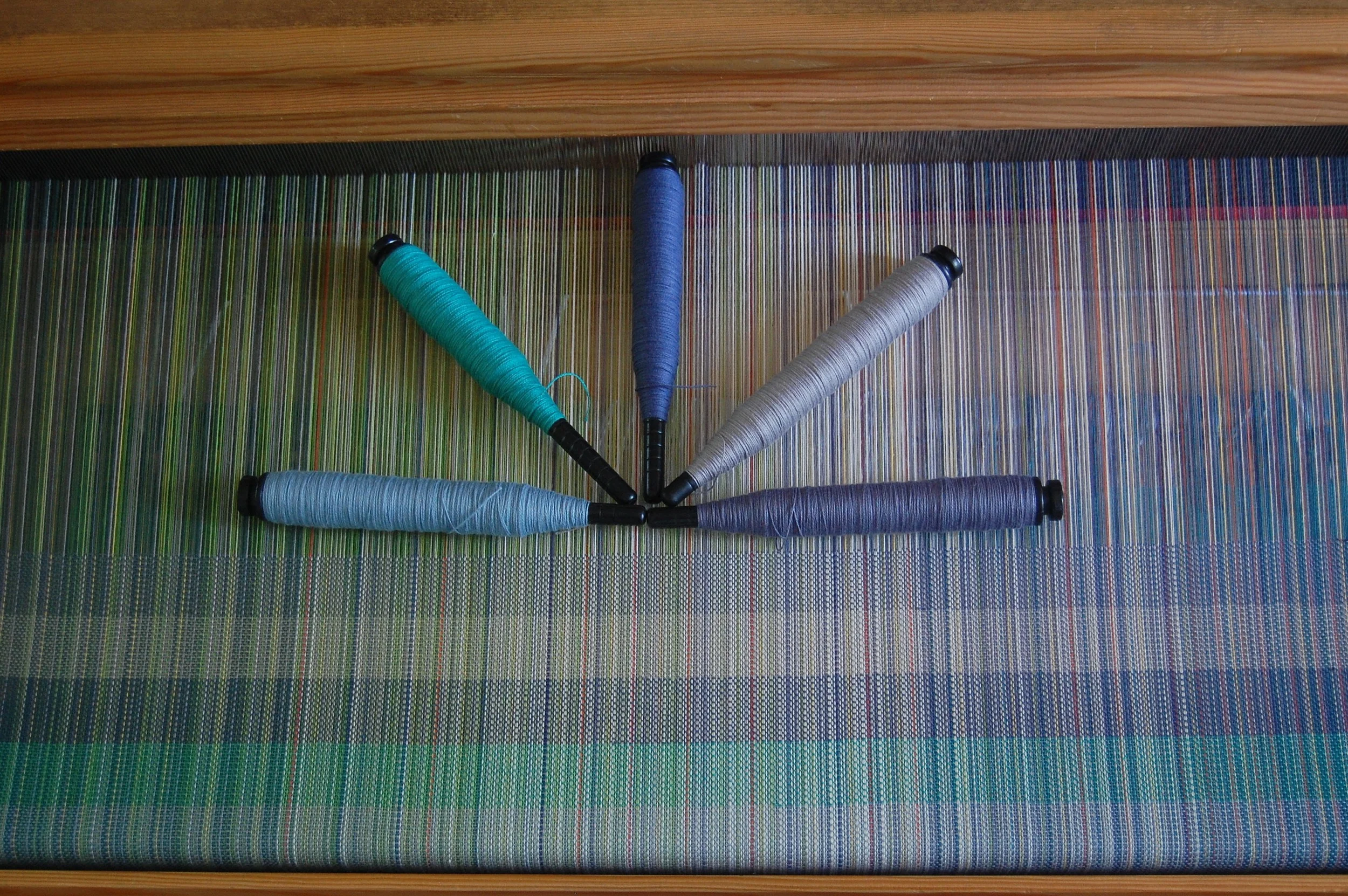 The cottons, from the bottom of the woven sample (and counterclockwise beginning with the pirn on the left: slate blue cotton, blue-green Egyptian cotton, denim blue cotton, medium grey Egyptian cotton, Steel-blue Egyptian cotton.